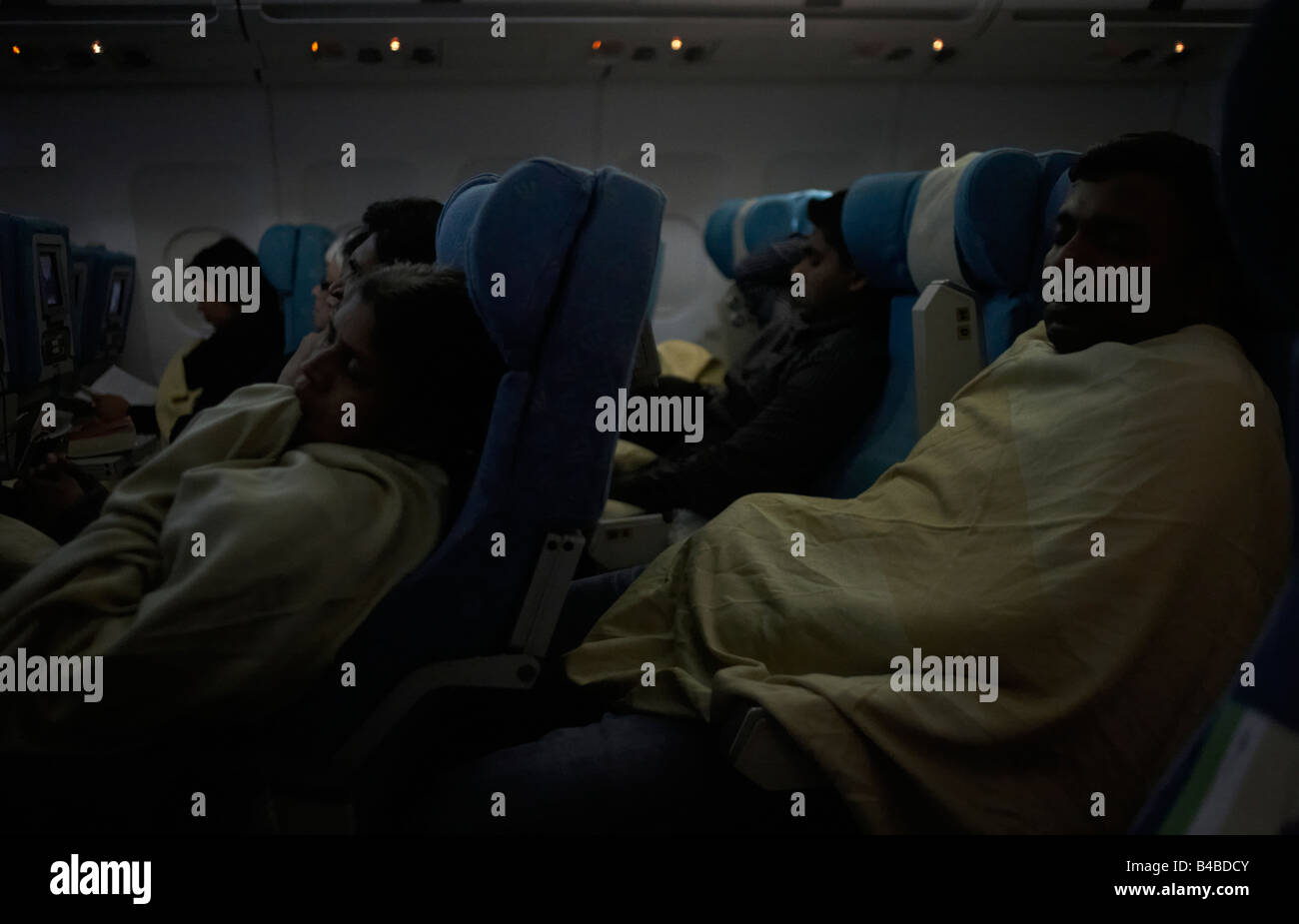 With cabin lights dimmed economy class passengers sleep under blankets on an international long-haul flight Stock Photo