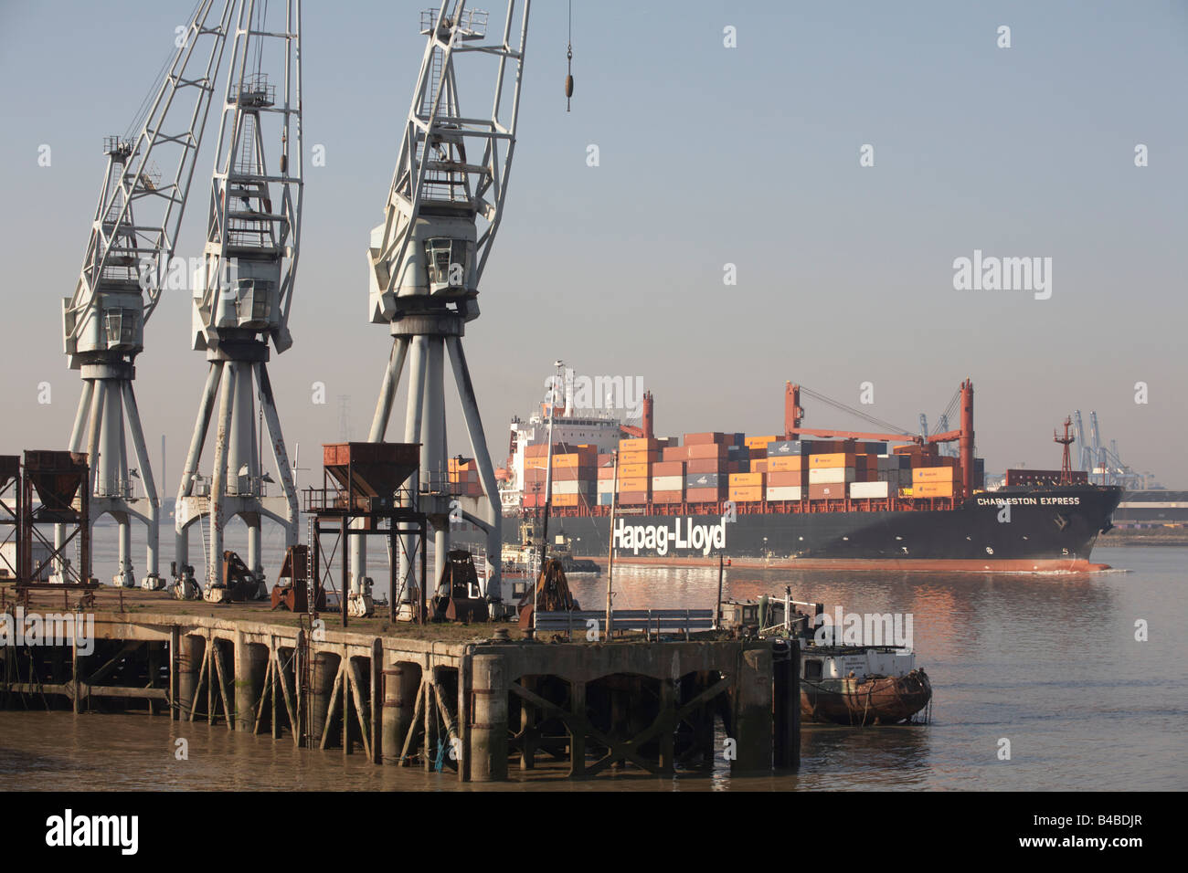 Giant cargo container ship on the River Thames eases downstream past old dock cranes at Gravesend, towards open sea at Southend Stock Photo