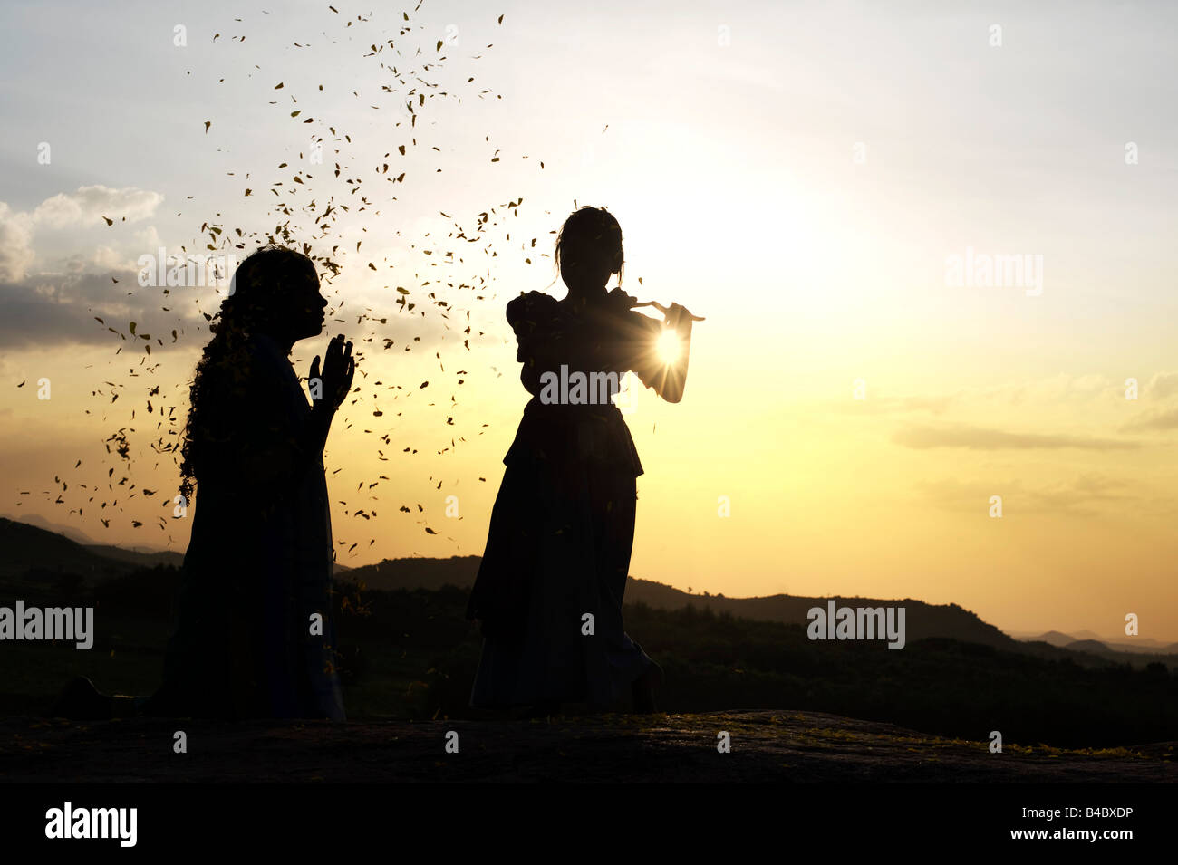 Two Indian sisters performing a hindu devotional dance on a rock at sunset silhouette. Andhra Pradesh, India Stock Photo