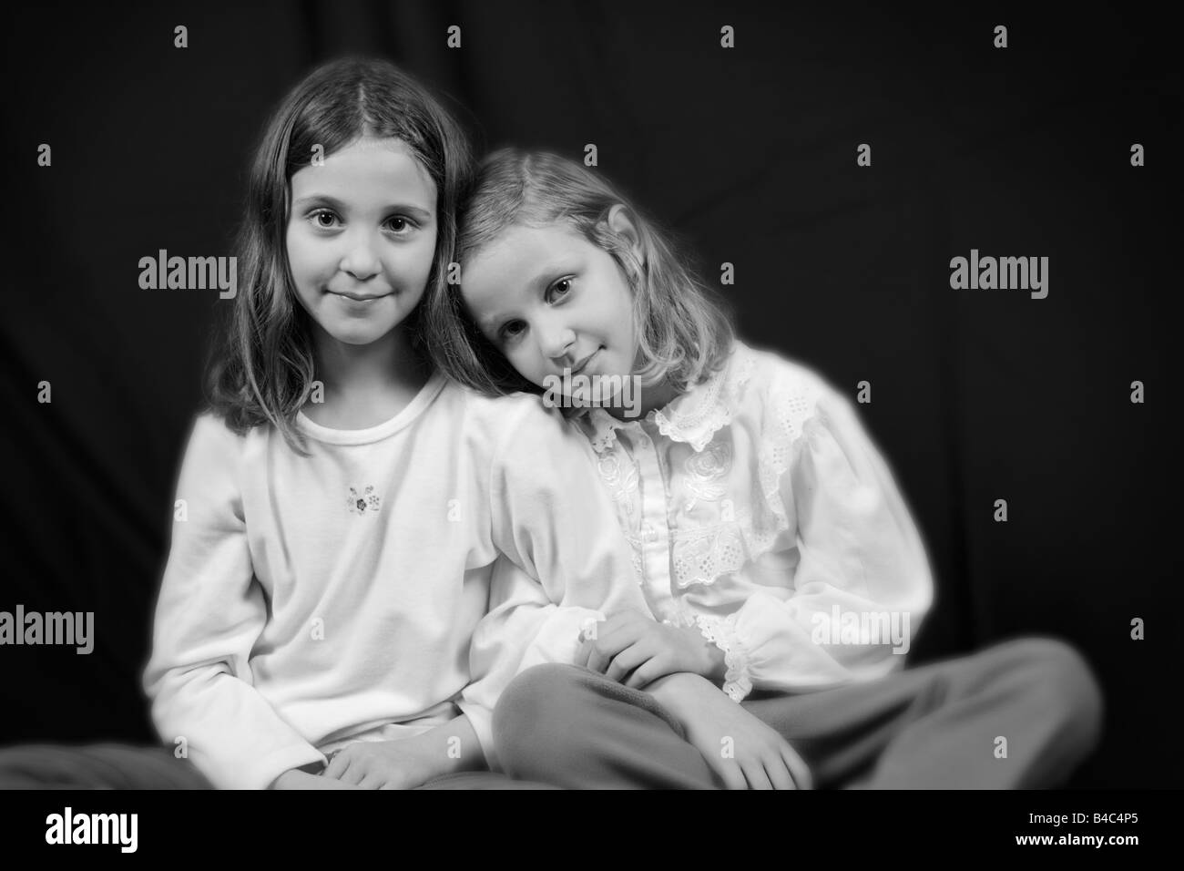 black and white portrait of two beautiful young girls holding each other on black background Stock Photo