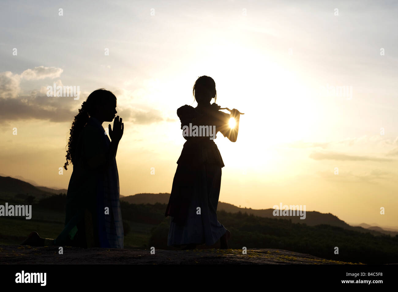 Two Indian sisters performing a hindu devotional dance on a rock at sunset silhouette. Andhra Pradesh, India Stock Photo