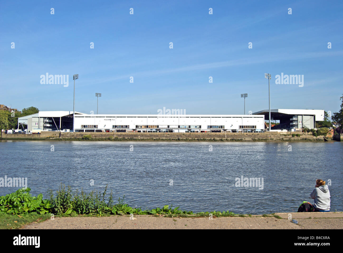 young woman sits by the river thames facing craven cottage, home of fulham football club, in southwest london, england Stock Photo