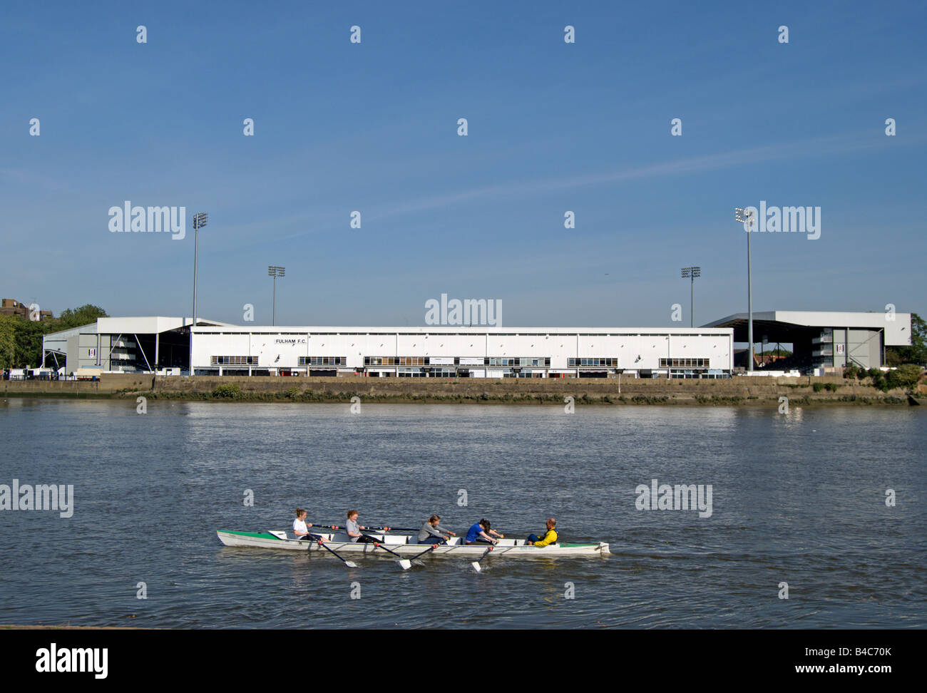 rowers on the river thames passing craven cottage, home of fulham football club, in southwest london, england Stock Photo