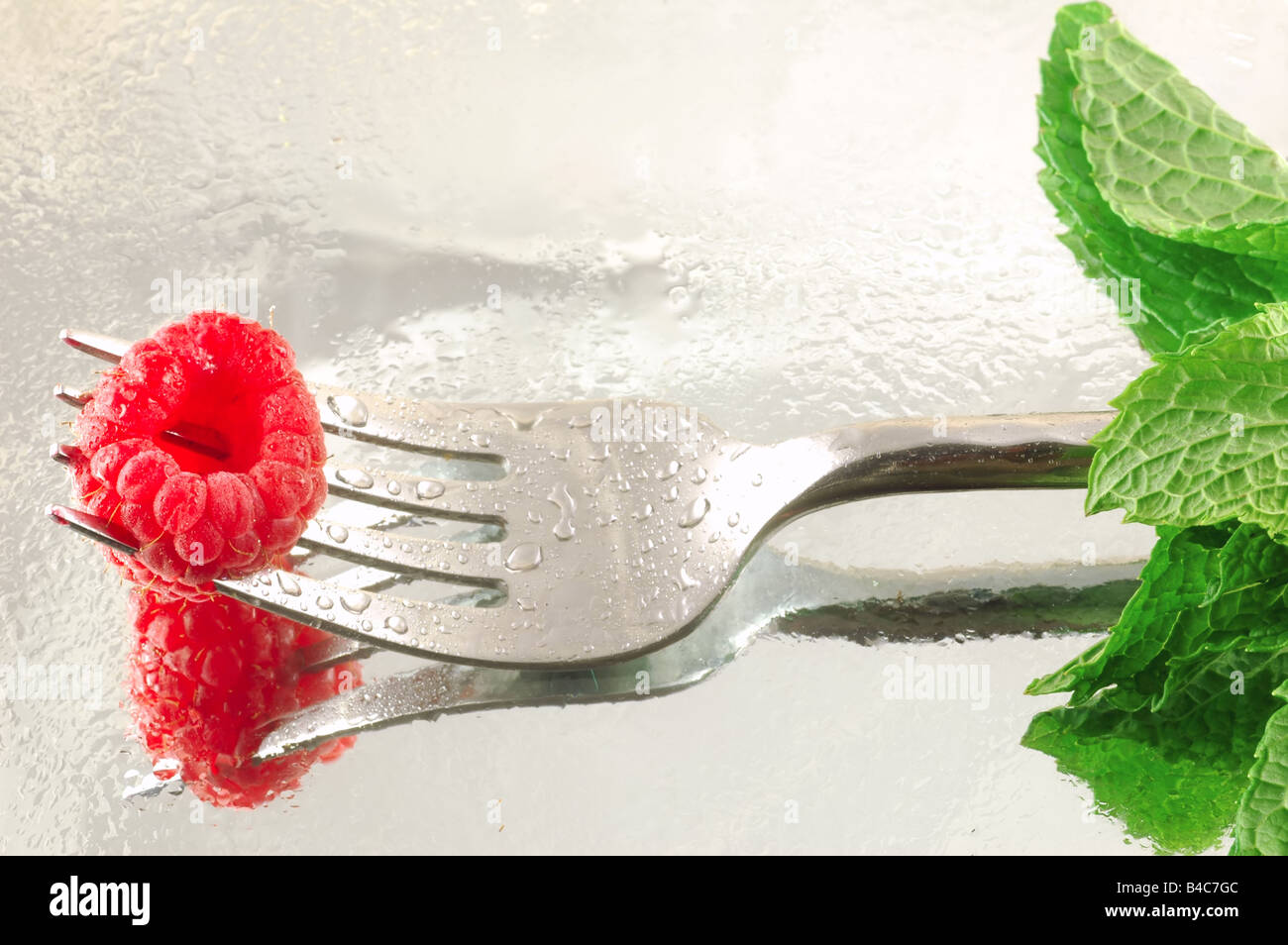 Fresh chilled raspberry on a fork with mint on a reflective background shaped like a long stem rose Stock Photo