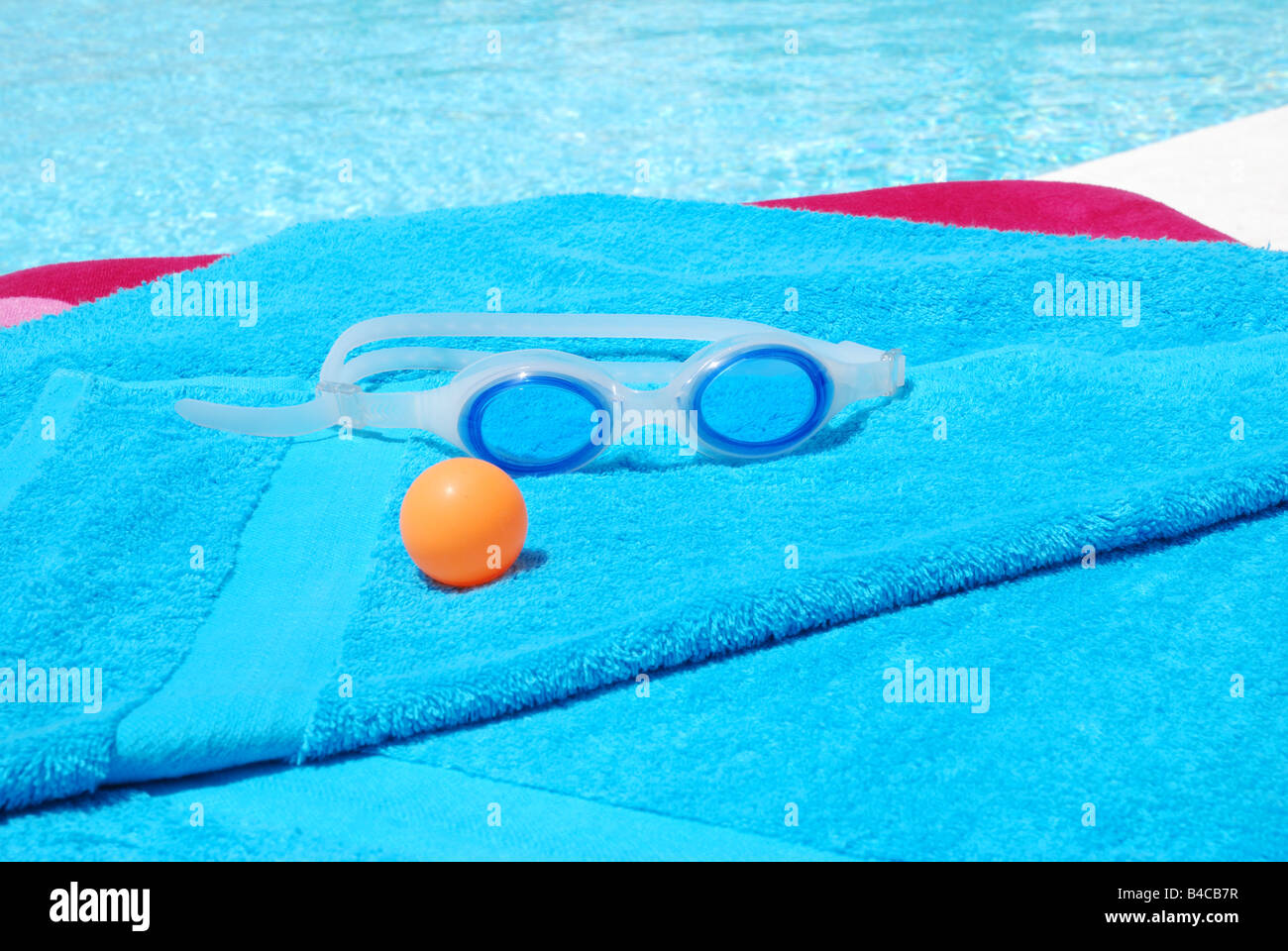 Goggles and orange ball on blue towel by the swimming pool. Stock Photo