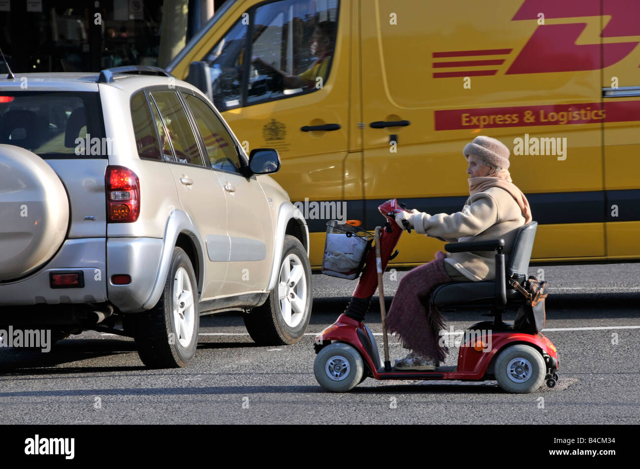 Older person driving mobility scooter between traffic and parked vehicles Stock Photo