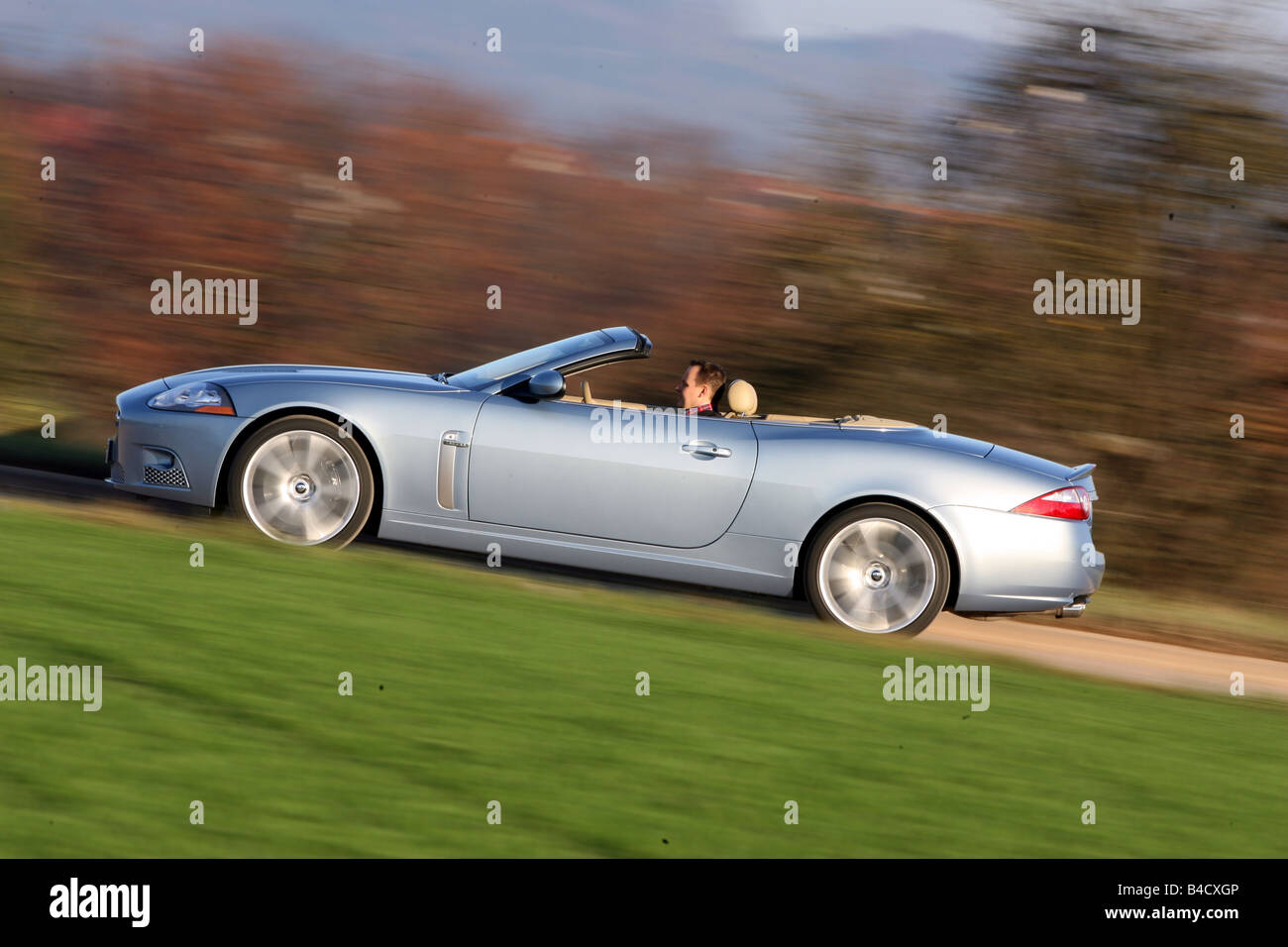 Jaguar XKR Convertible, model year 2006-, silver, driving, side view, country road, open top Stock Photo