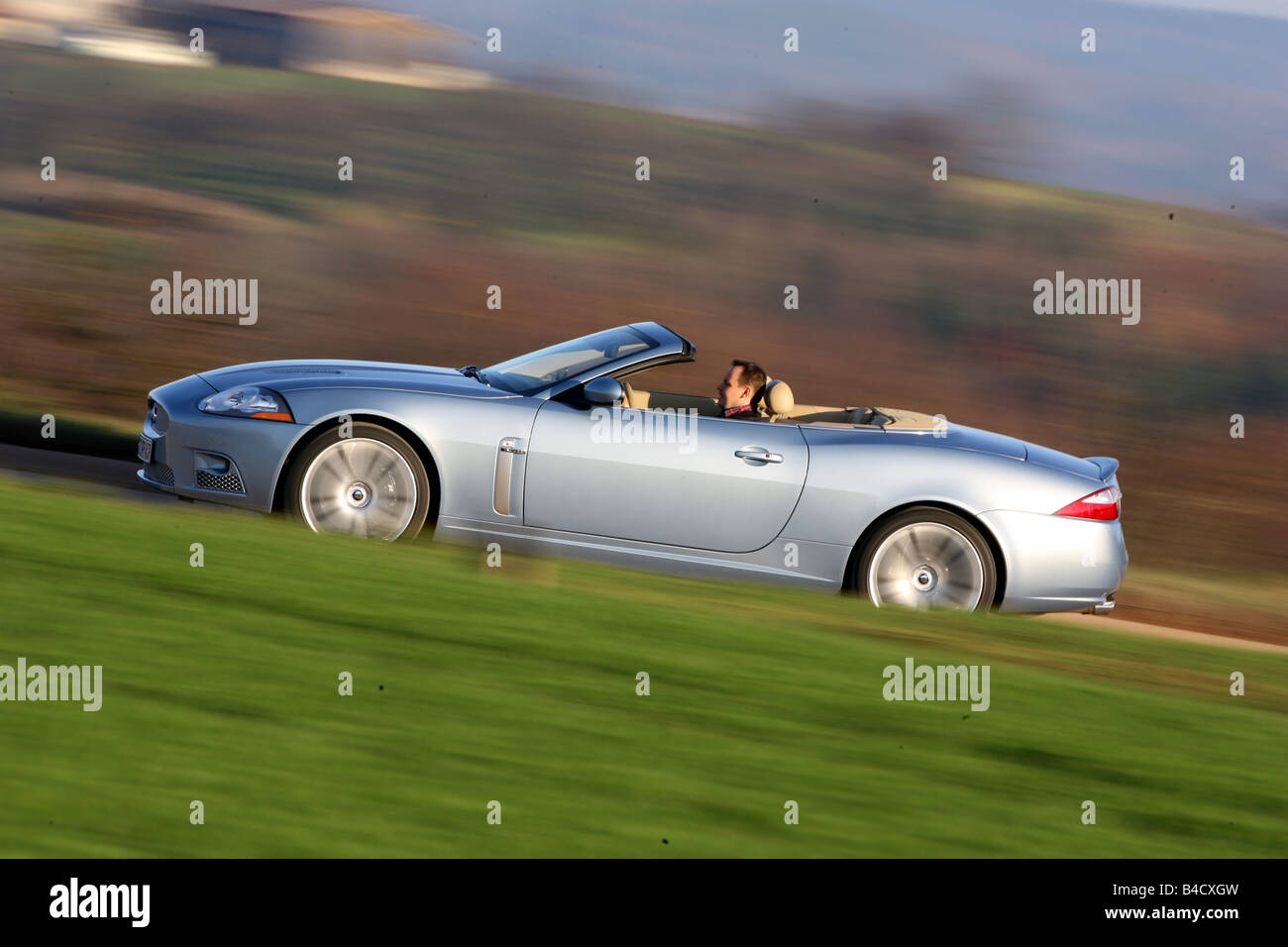 Jaguar XKR Convertible, model year 2006-, silver, driving, side view, country road, open top Stock Photo