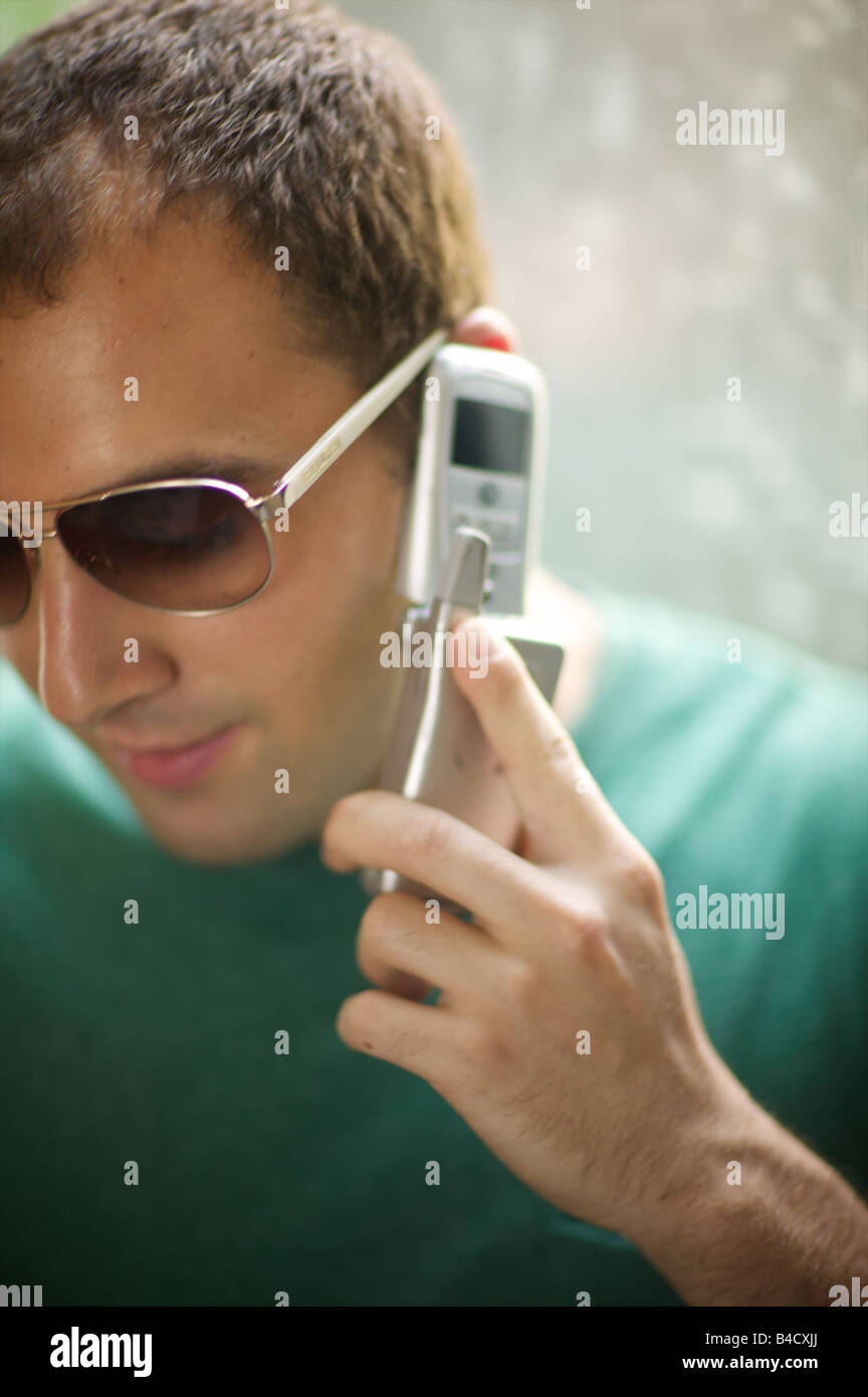 Unbearably hip german guy in aviator shades and green t shirt tries to rustle up a little action on his new Motorola cellphone. Stock Photo