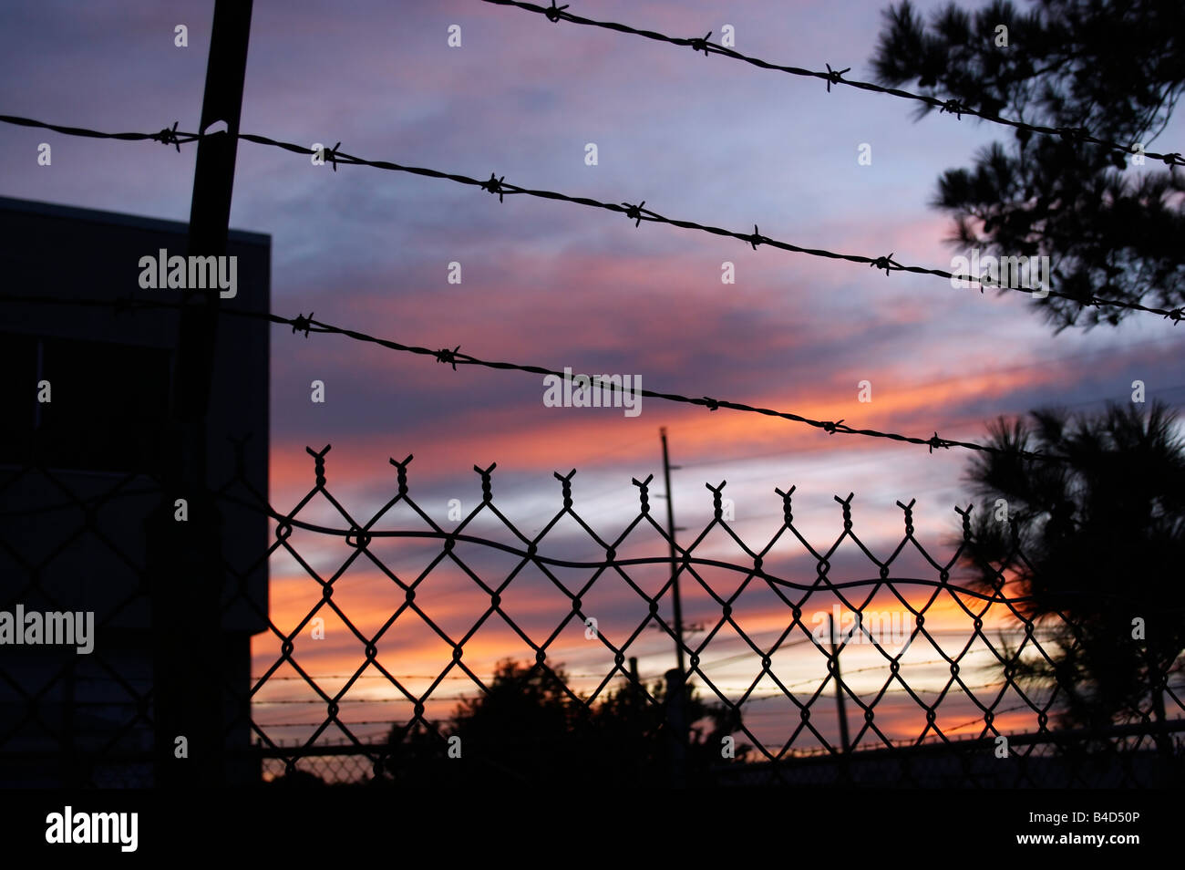 A chain link fence and barbed wire surrounds an industrial warehouse in Cambridge Maryland at sunset Stock Photo