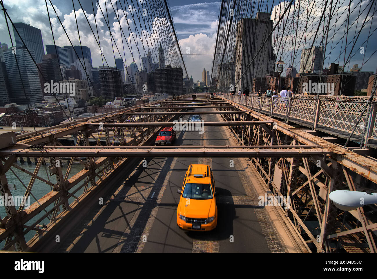 A taxi is among the traffic crossing the Brooklyn Bridge.  Pedestrians can also be seen on the upper walkway. Stock Photo