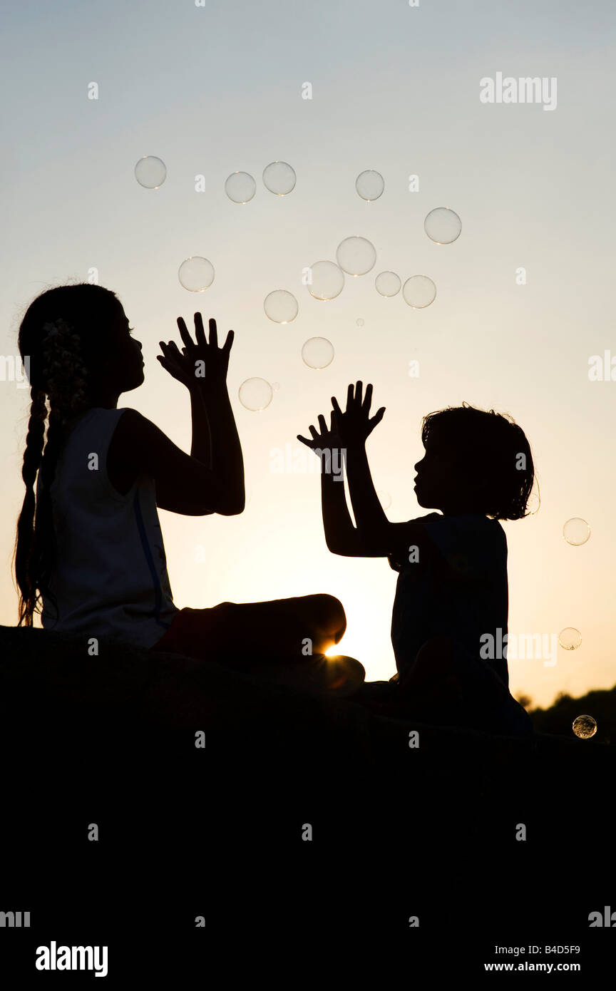Two indian girls sitting on a rock playing with bubbles silhouette ...
