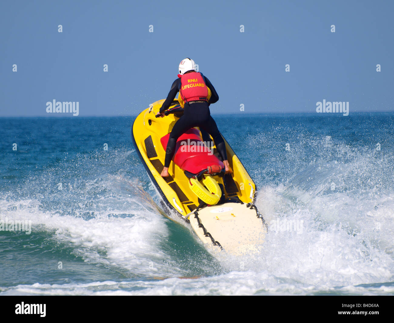 RNLI Lifeguard on a rescue jetski splashing through a wave Stock Photo ...