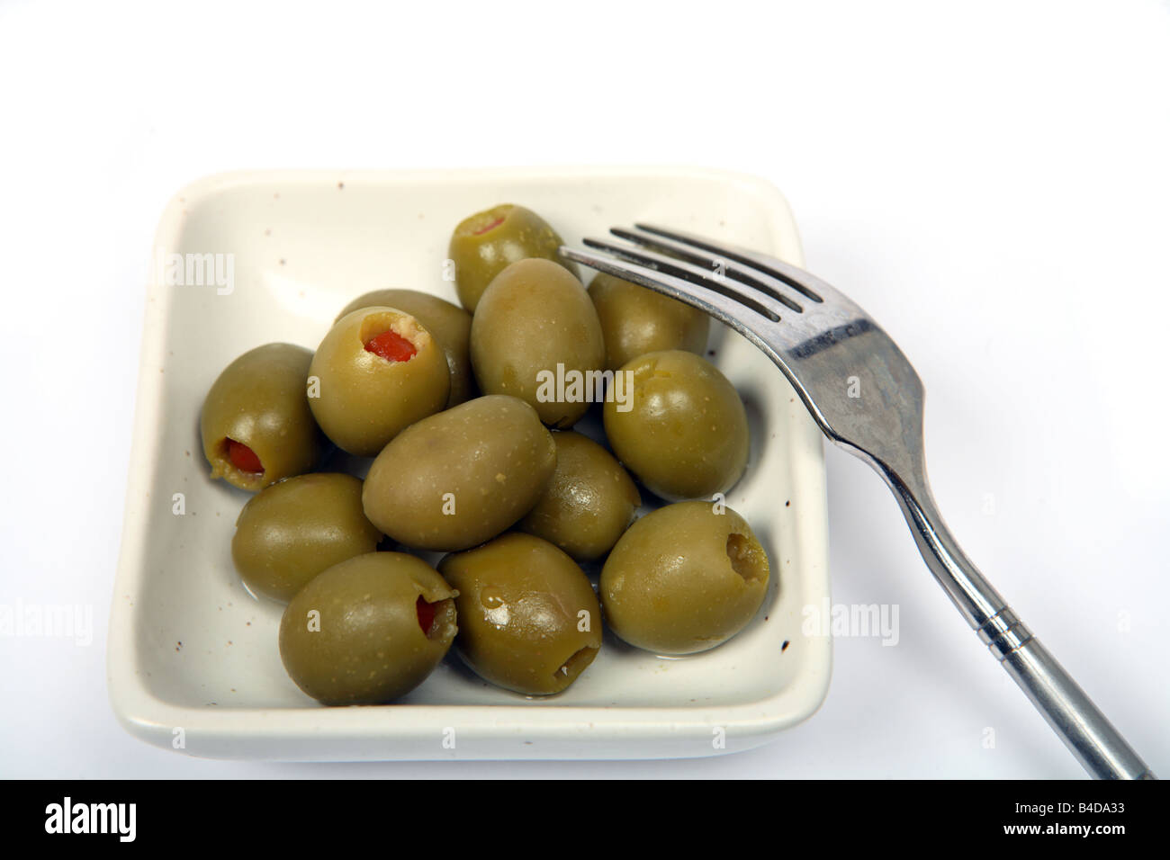 A speckled bowl of pimento stuffed green olives over a white background with a small fork Stock Photo
