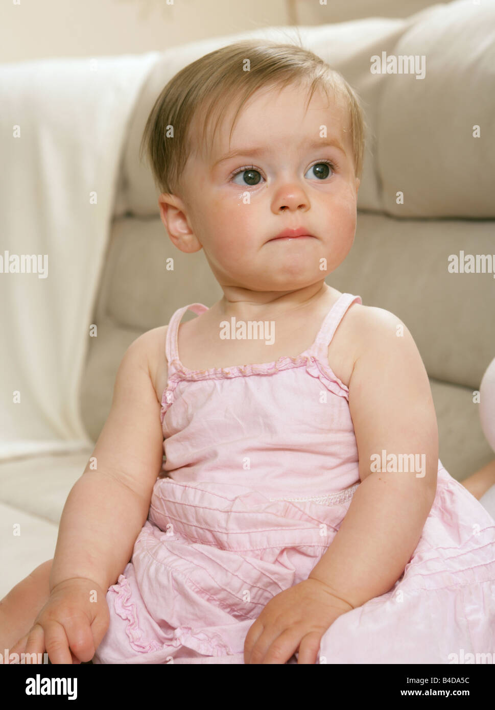 A nine month old girl sitting down with a sad face after crying Stock