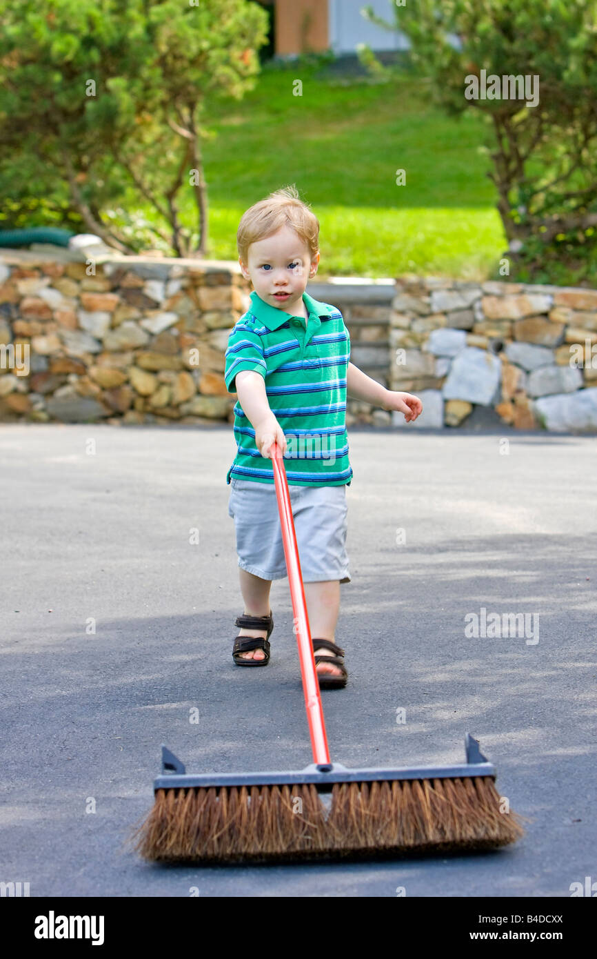 Boy with yard brush cleaning driveway outside Stock Photo Alamy