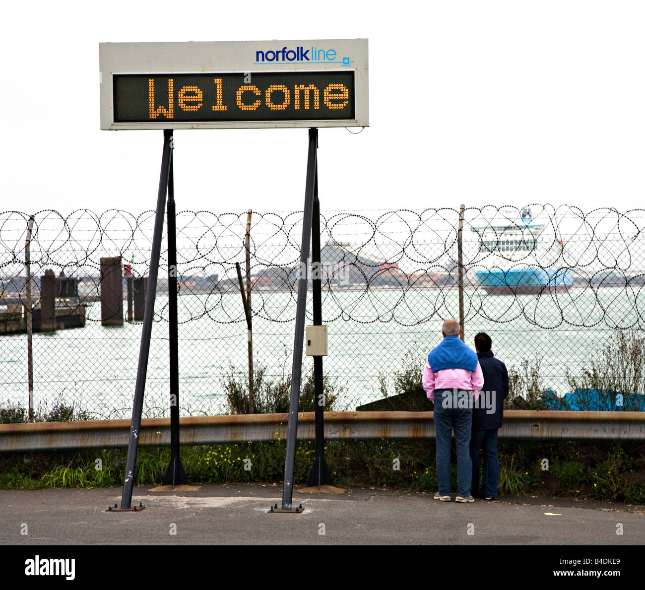 People standing behind security fence with welcome sign at ferry terminal Dunkirk France Stock Photo