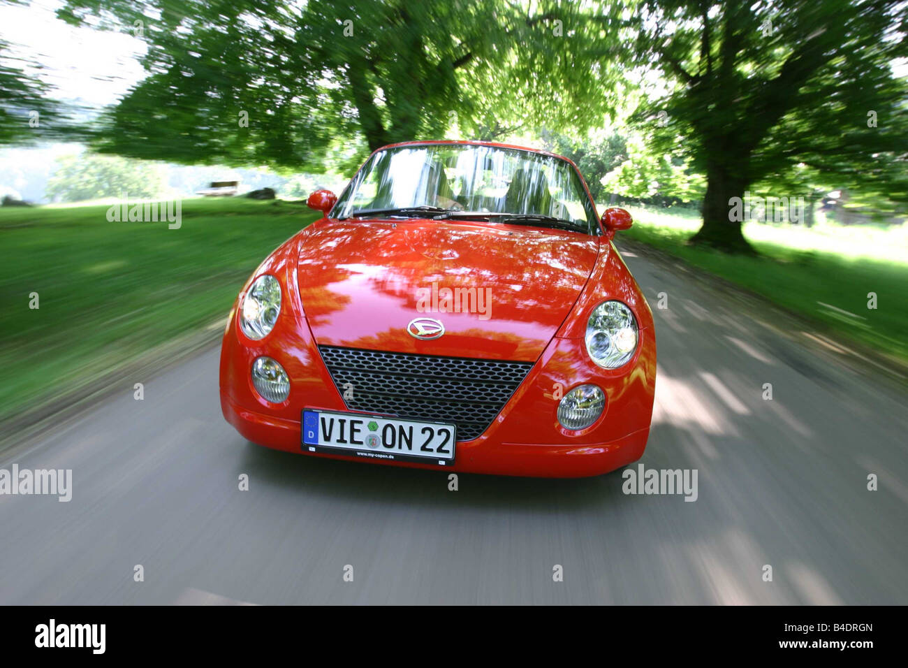 Car, Daihatsu Copen, Convertible, model year 2003-, red-orange , open top, driving, country road, diagonal from the front, Front Stock Photo
