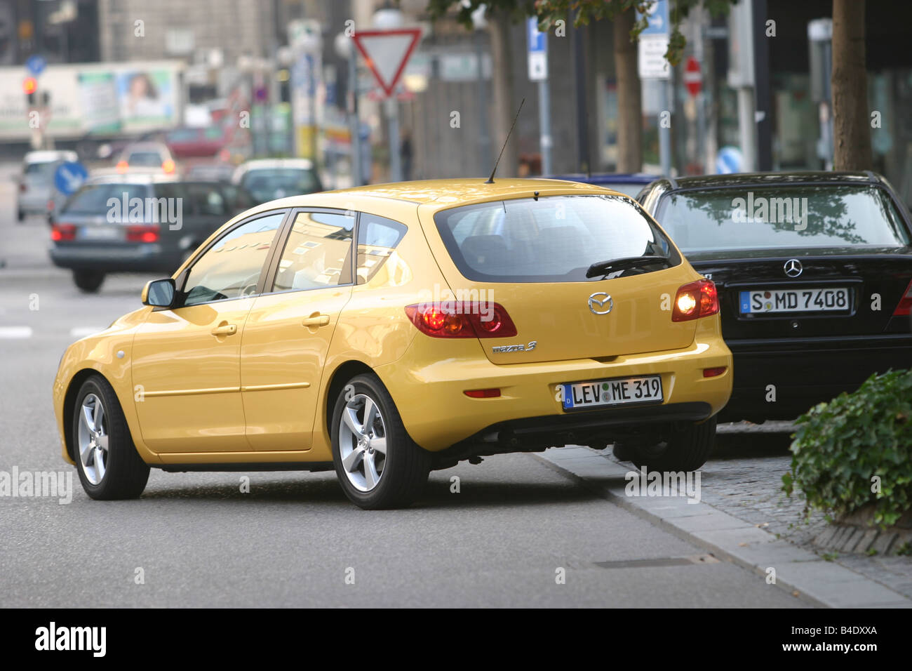 Car, Mazda 3 Sport 1.6, Lower middle-sized class, Limousine, model year 2003-, FGHDS, yellow, driving, diagonal from the back, r Stock Photo