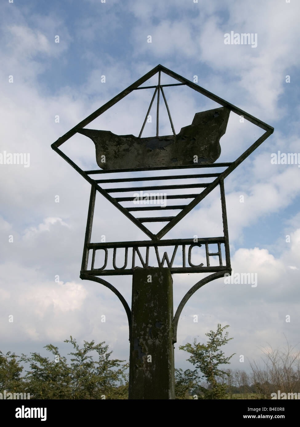 A metal sign with a ship motif for the village of Dunwick Suffolk UK dark against the sky Stock Photo