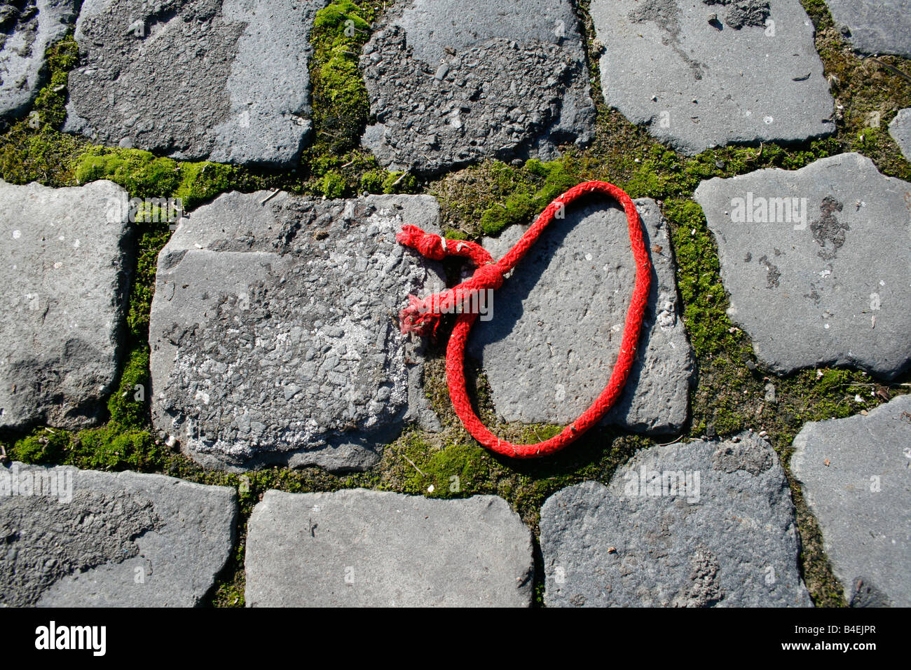 one piece of red string on cobbles pavement outdoors Stock Photo - Alamy