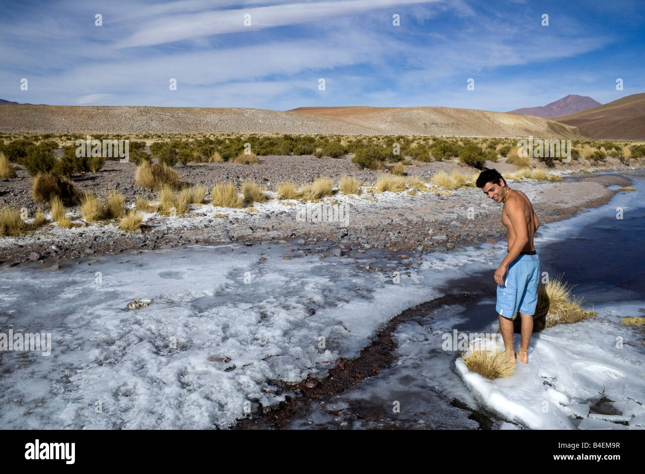 A backpacker tests the temperature of the water of a frozen stream at high altitude in the Andes in Southwest Bolivia Stock Photo