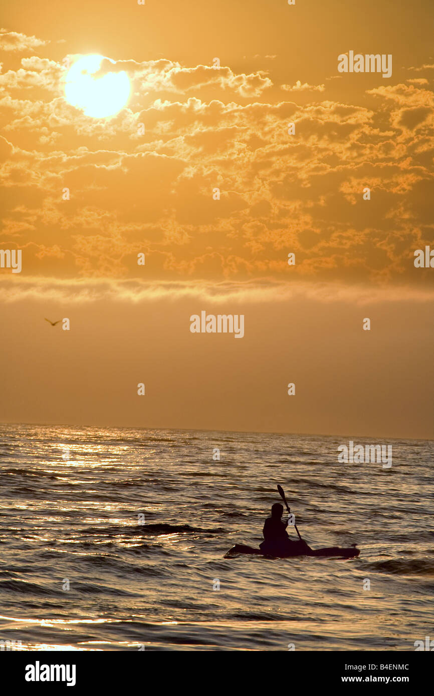 A silhouette of a kayaker riding waves of the ocean at sunset. Stock Photo