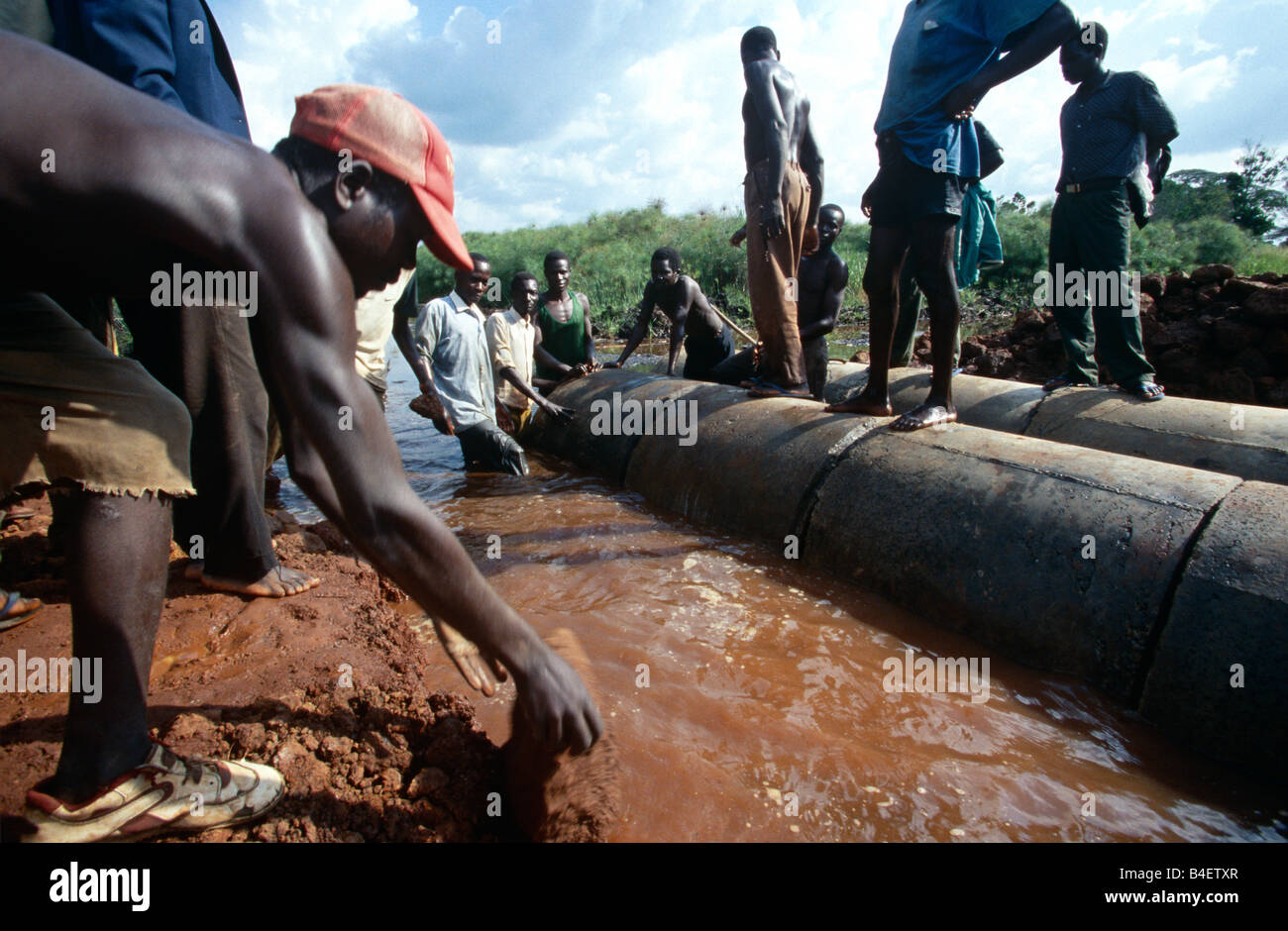 Team of workers connecting industrial pipes in rural waterway, Uganda