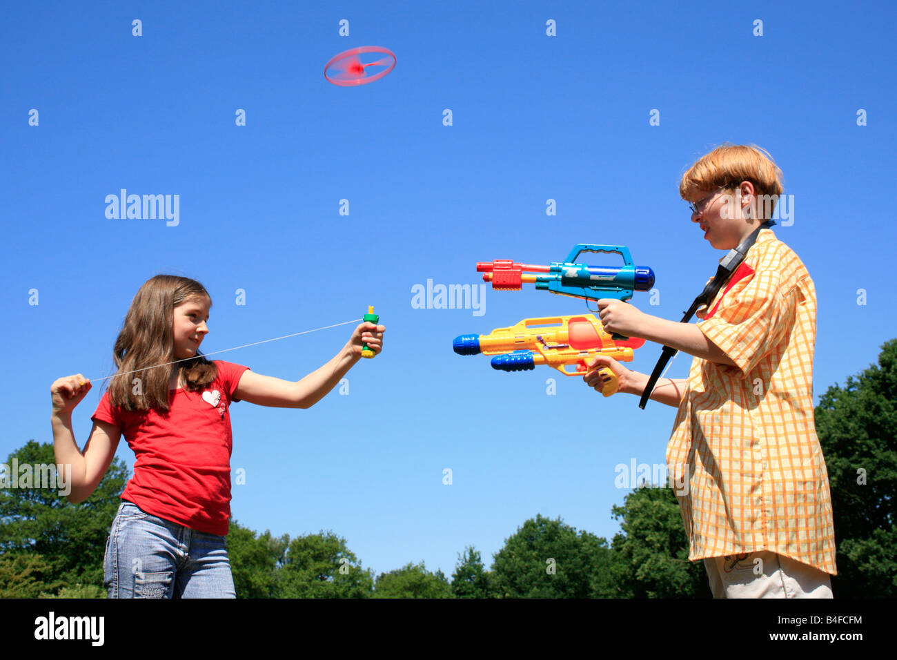 a young girl is playing with a toy helicopter while her brother is playing with toy guns Stock Photo