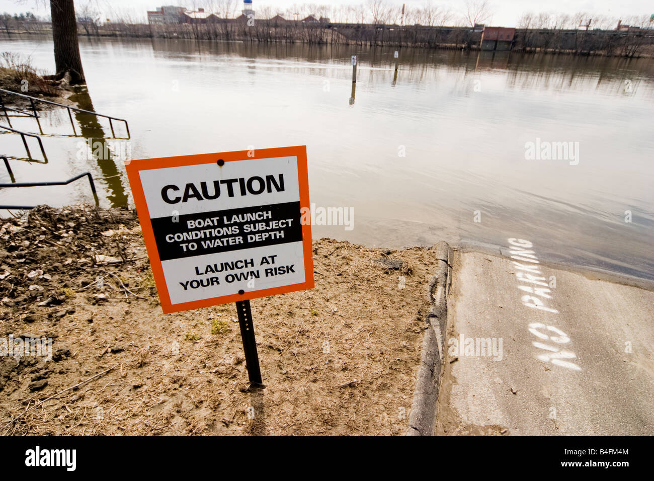 CAUTION sign near a boat launch at an overflowing river Stock Photo