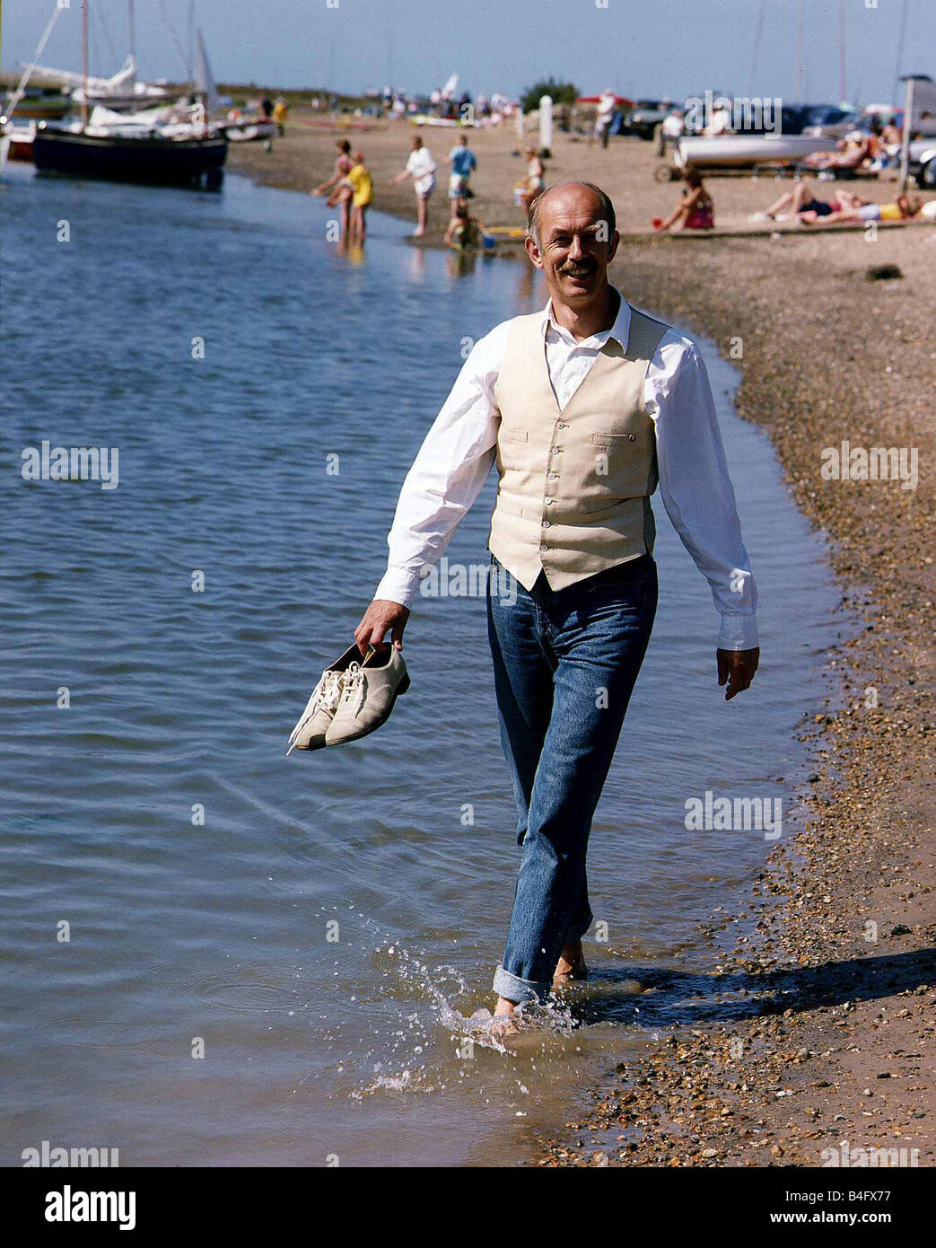Roy Marsden actor walking along beach paddling in water and holding shoes DBase Mirrorpix Stock Photo