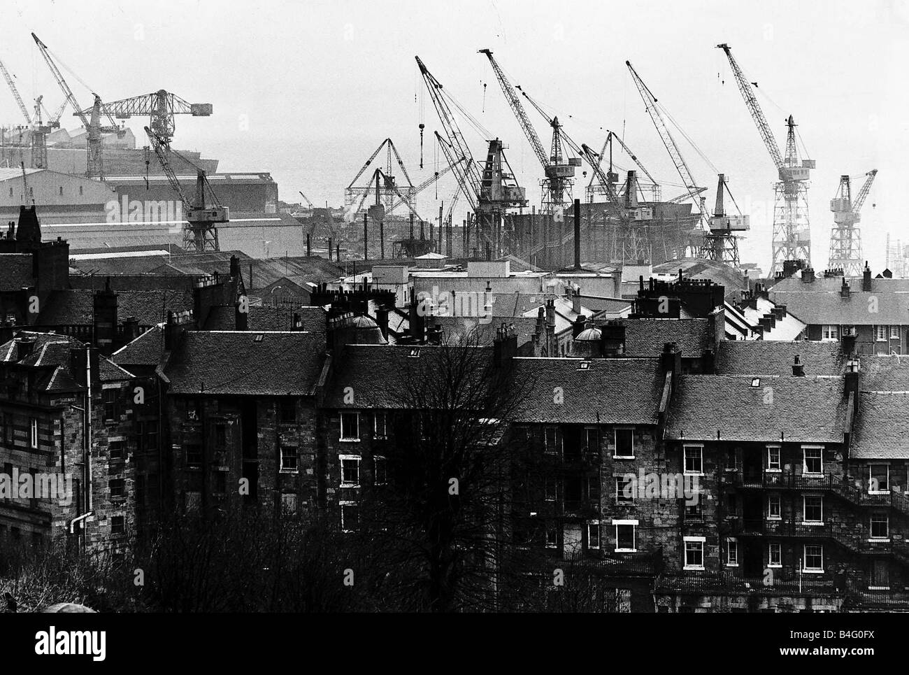 Shipyard cranes rise above tenement apartment buildings by the River Clyde in Scotland March 1971 Stock Photo