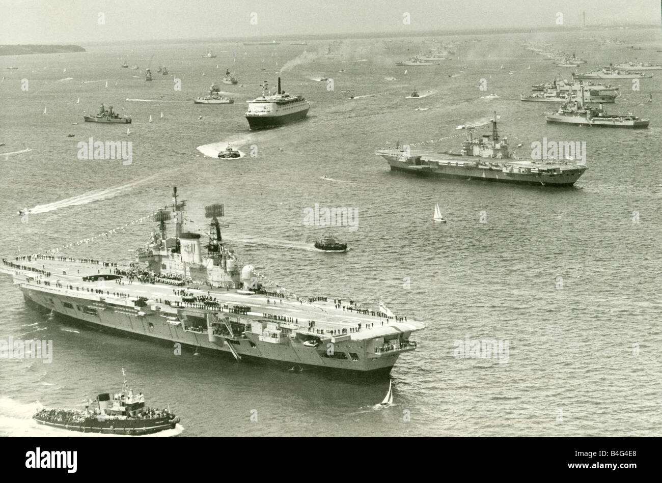 The Cunard liner QEII cruises through the fleet of Royal Navy ships gather at Spithead for the Queens silver jubilee review In the foreground the Aircraft Carriers HMS Ark Royal and HMS Hermes June 1977 Stock Photo