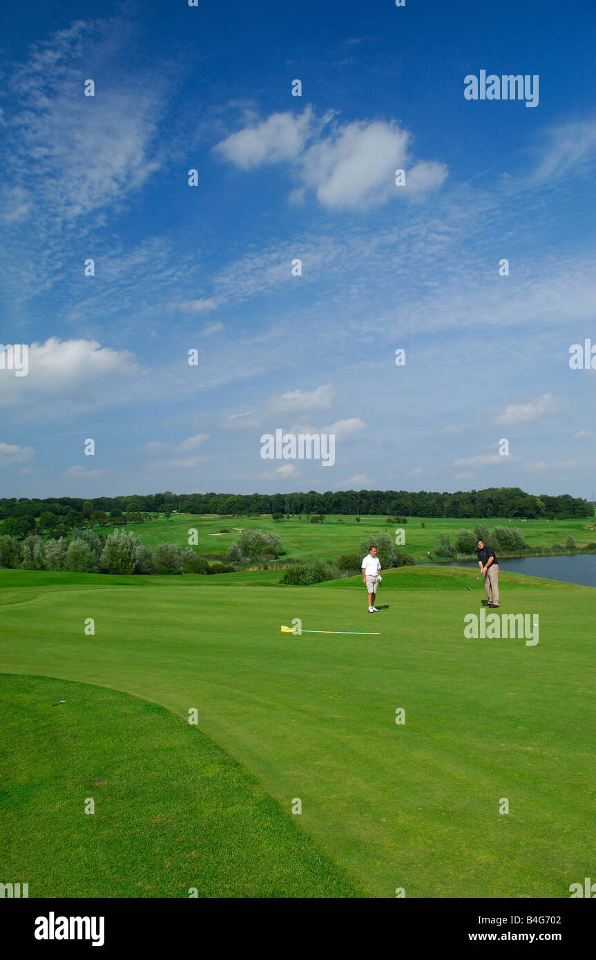 A green golf course with 2 golfers on blue sky - France Stock Photo