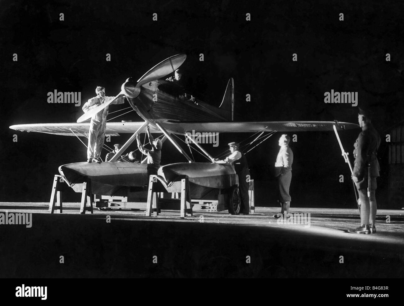 R J Mitchell Aircraft Designer August 1929 Working by searchlight on the Supermarine S6 engine at 10pm at night Reginald Mitchell the designer in his plus fours trousers seen at the right oversees work being carried out on the seaplane An armed guard stands nearby with his rifle and bayonet Stock Photo