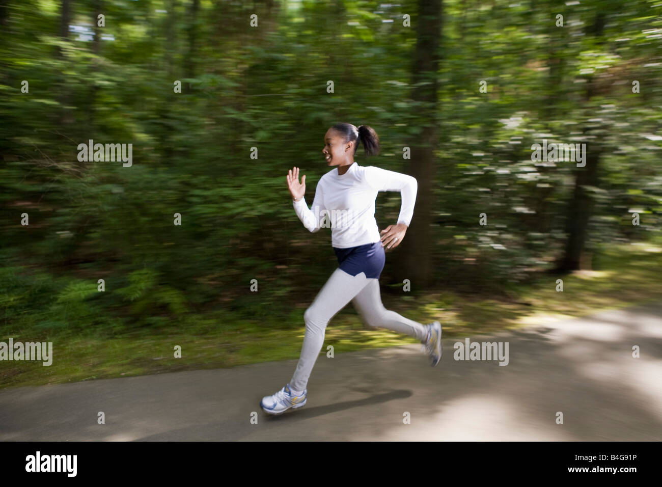 A woman jogging through a wooded park Stock Photo