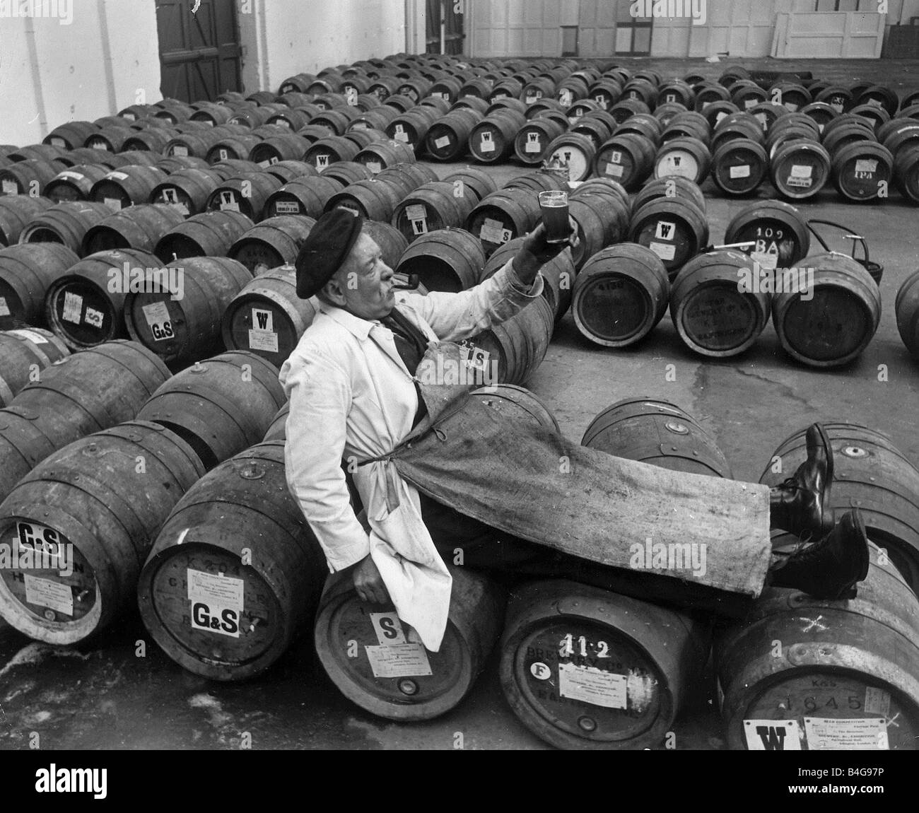 Brewery Barrels of Beer Harry Meyer lays across the top of Beer Barrels holding a pint of beer and smoking a pipe Stock Photo