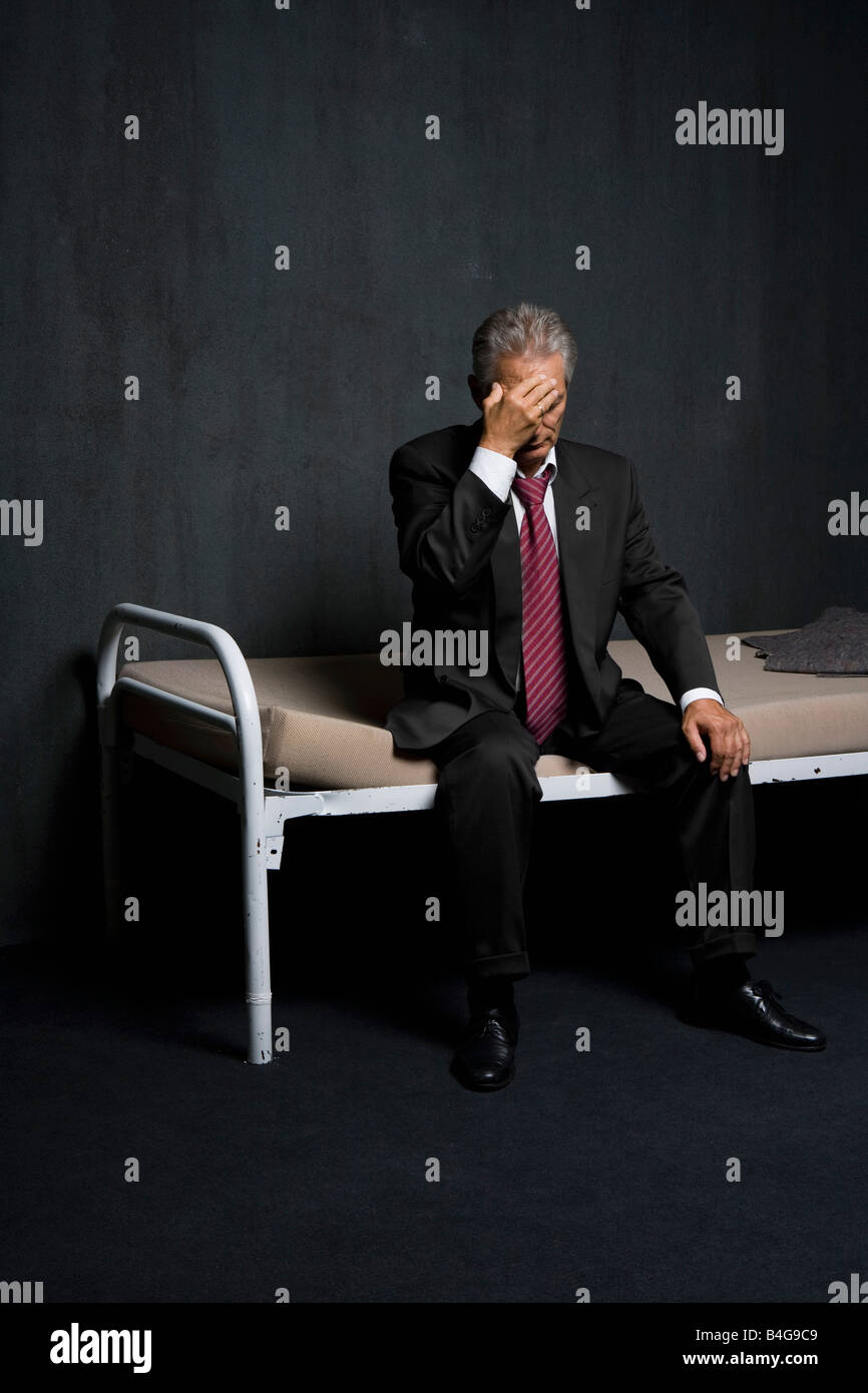 A business man sitting on a bed in a prison cell Stock Photo