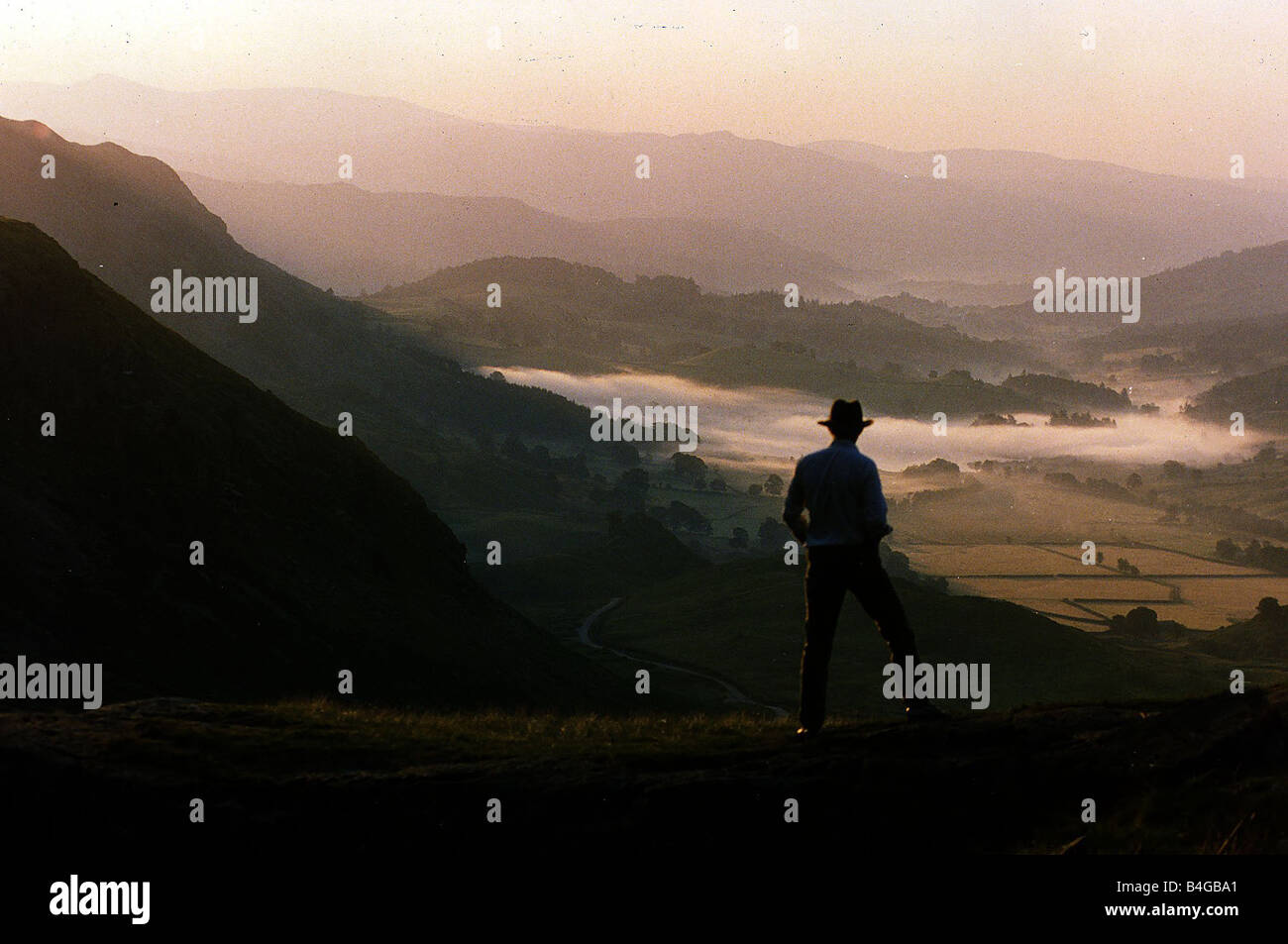 Lake District dawn rises in a lakeland pass watched by man in hat Stock Photo