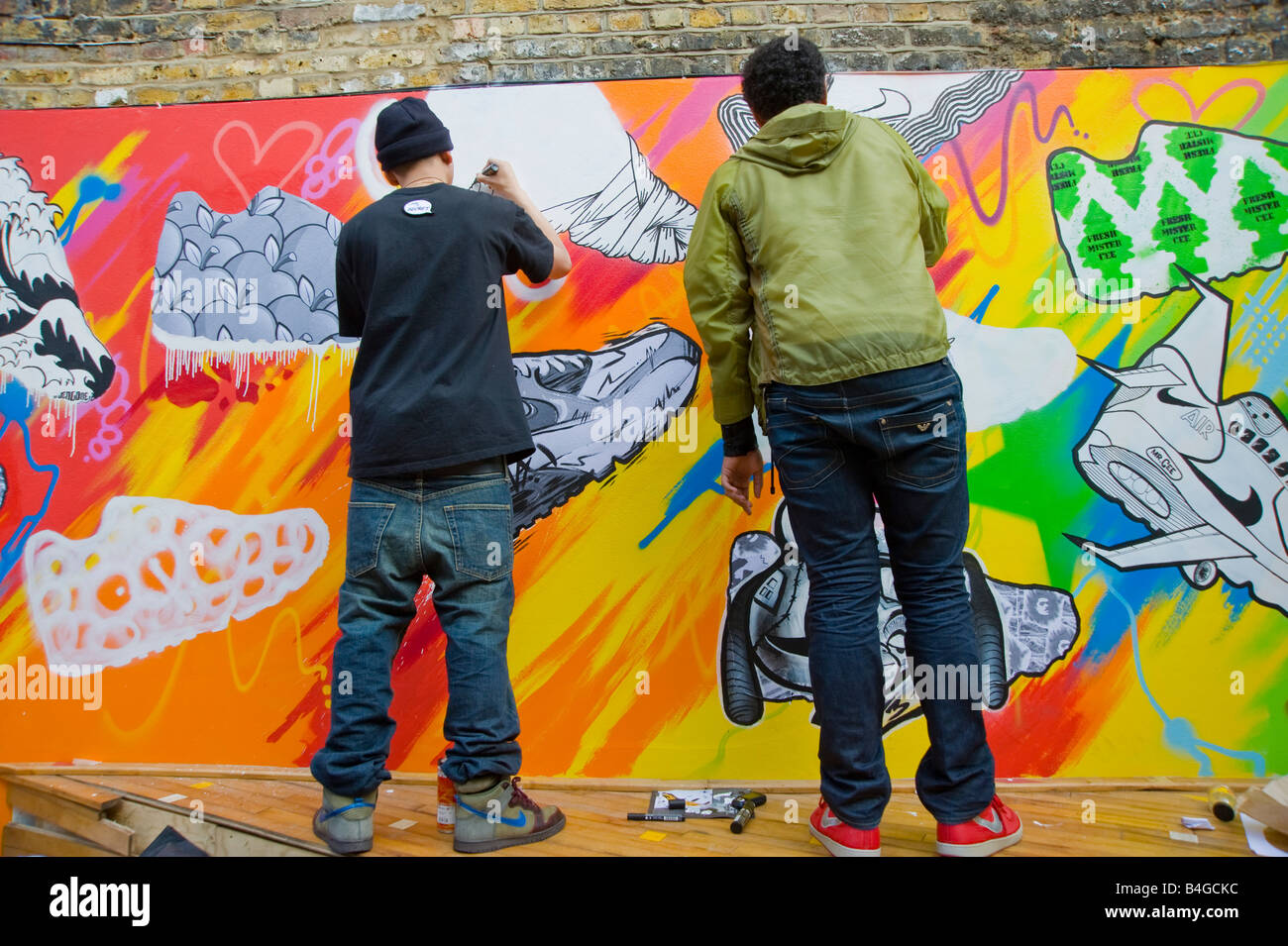 Two Young men painting a large mural of Nike 90 trainers on a wall at the Nike  shop in Hoxton Hackney East London Stock Photo - Alamy