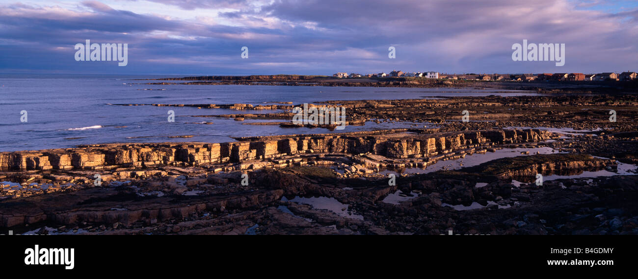 Beadnell, Northumberland, UK. View across the beach towards village with rock ledge in the foreground in evening light in August Stock Photo