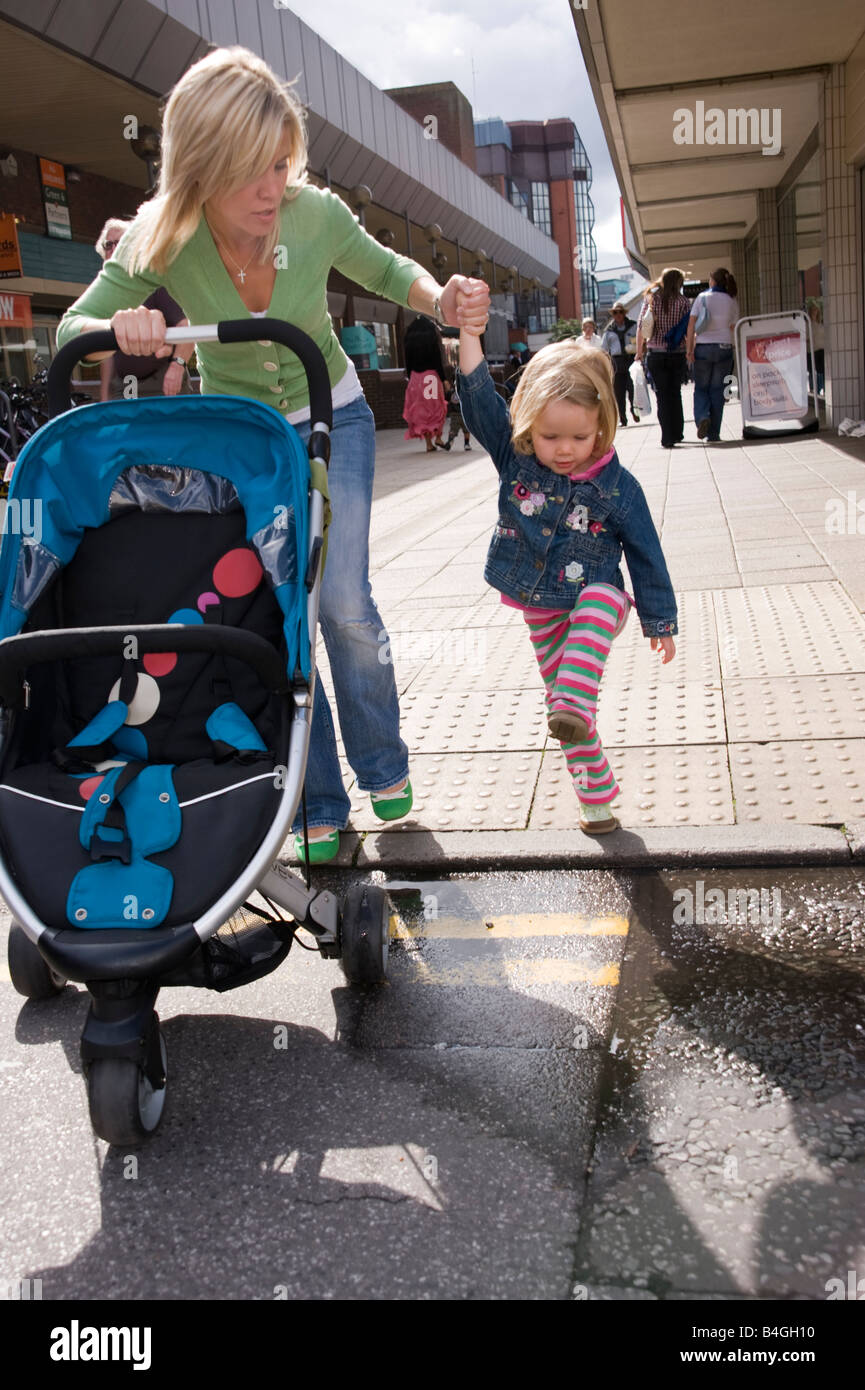 mother walking in a shopping centre holding her daughter s hand and pushing a buggy Stock Photo