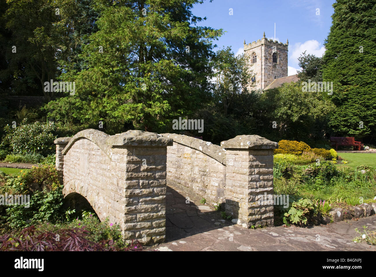 Bridge in Coronation gardens in the village of Waddington Lancashire with St Helens Church in the background Stock Photo
