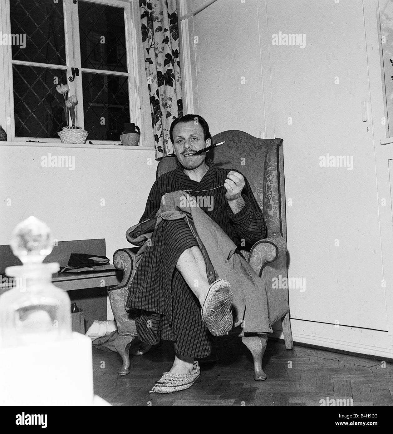 Actor Terry Thomas sitting at home sewing his coat February 1957 Stock