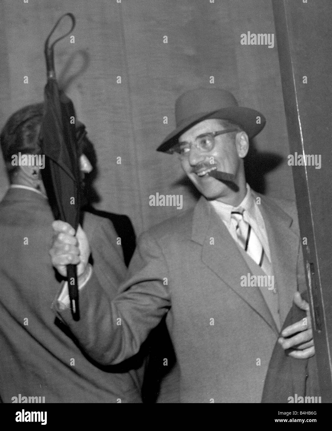 Comedian actor Groucho Marx one of the famous Marx Brothers enters the Savoy hotel in London smoking a Cigar and waving an umbrella June 1954 Stock Photo