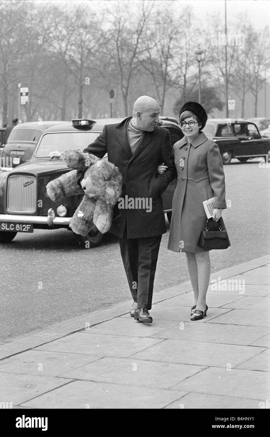 Actor Telly Savalas walking arm in arm in London with his wife Marilynn Gardner carrying a large big teddy bear under one arm February 1968 1960s Mirrorpix Stock Photo