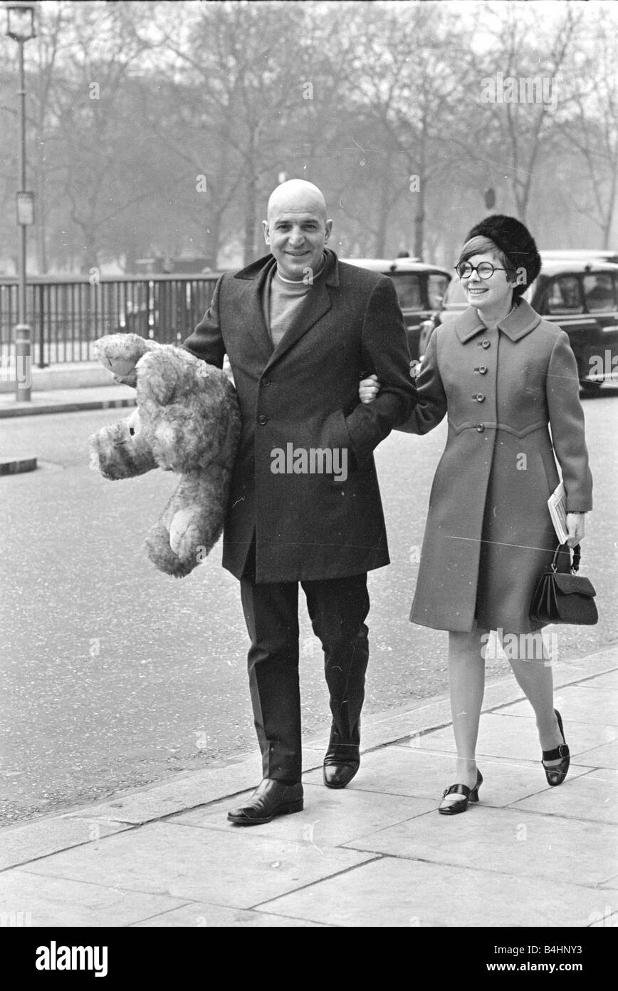 Actor Telly Savalas walking arm in arm in London with his wife Marilynn Gardner carrying a large big teddy bear under one arm February 1968 1960s Mirrorpix Stock Photo