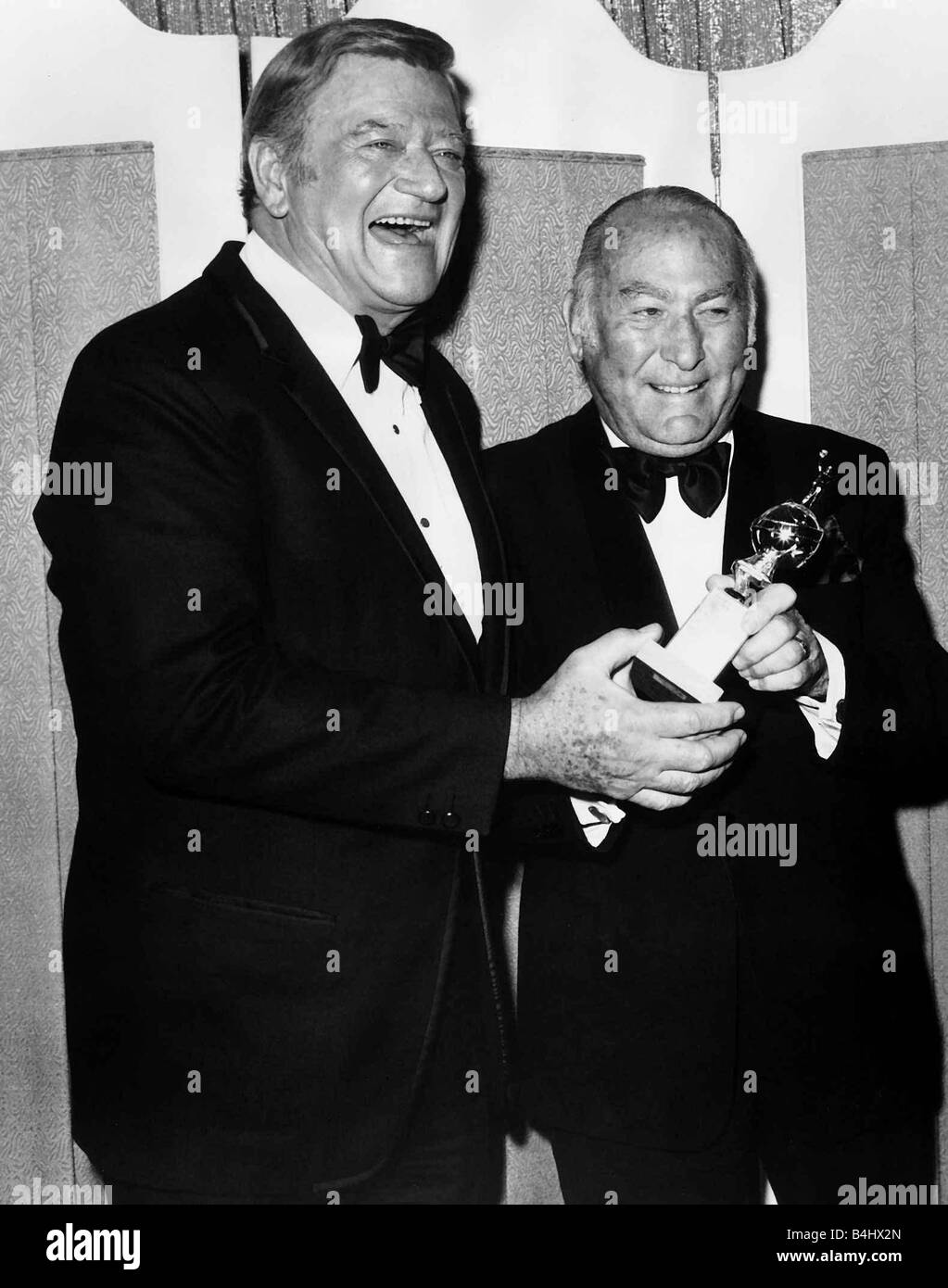 Hal Wallis film producer accepts Cecil B De Mille award 1975 from actor John Wayne Stock Photo
