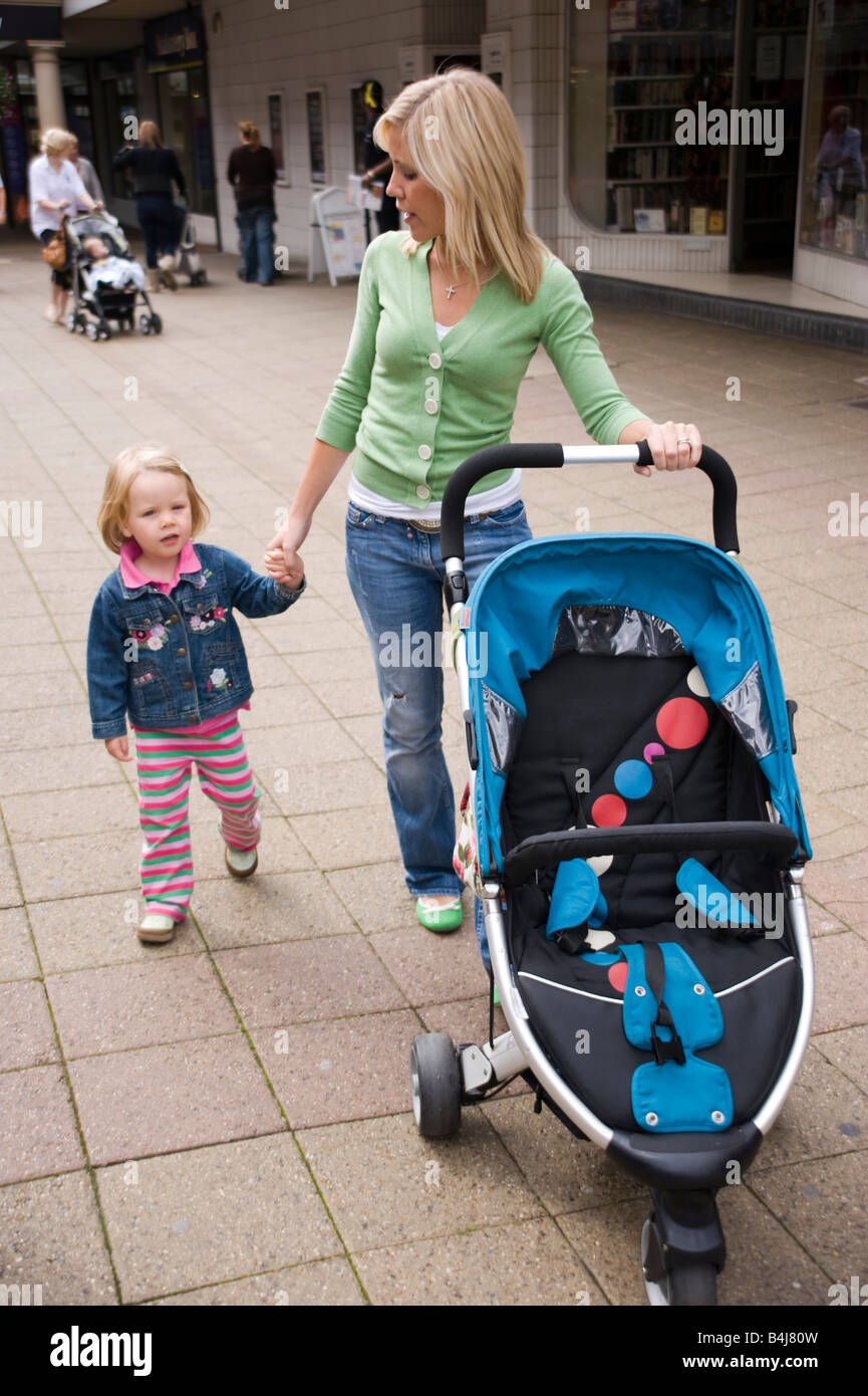 mother walking in a shopping centre holding her daughter s hand and pushing a buggy Stock Photo