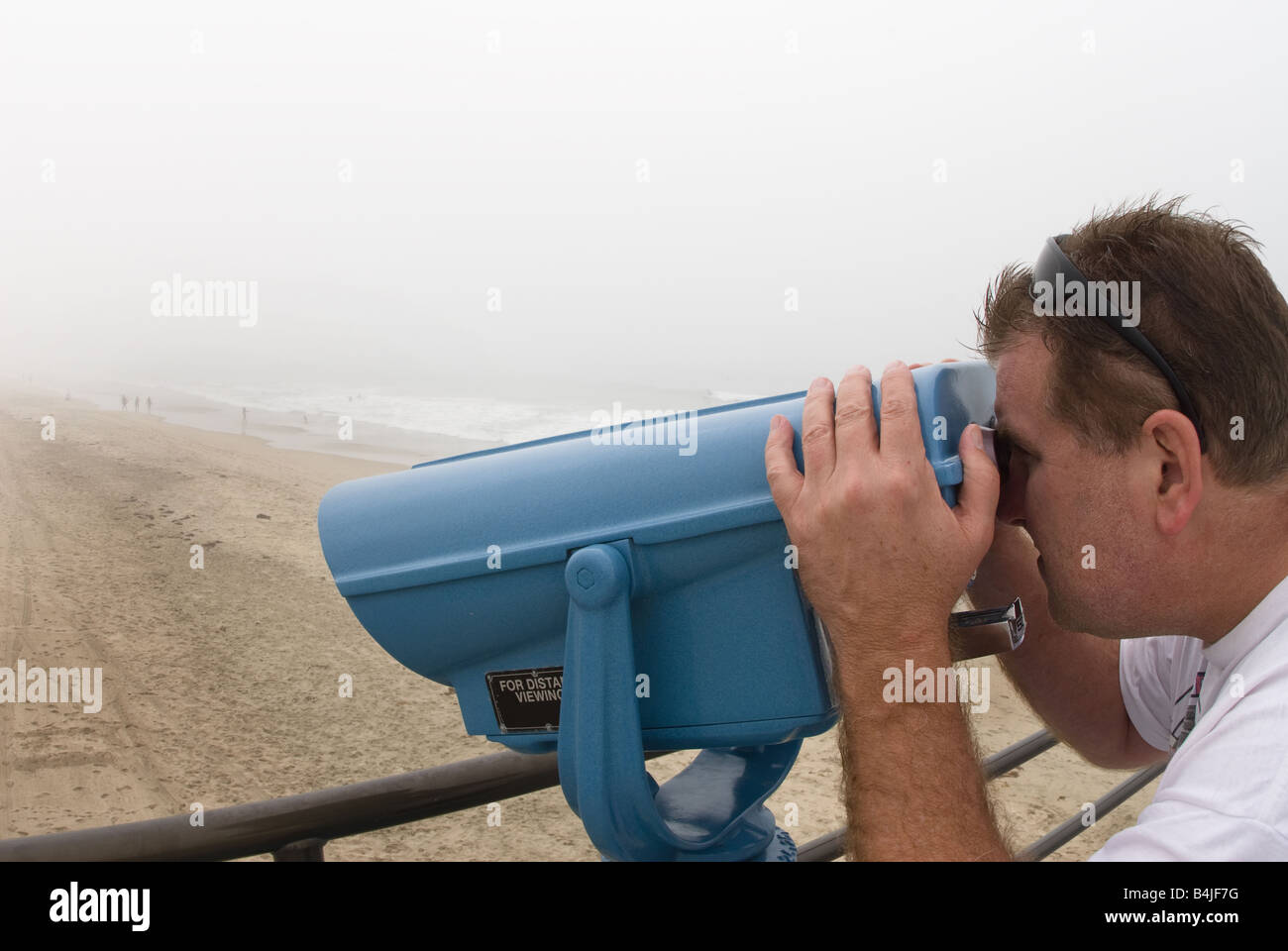A man views beachgoers through a pay per view telescope on a pier Stock Photo